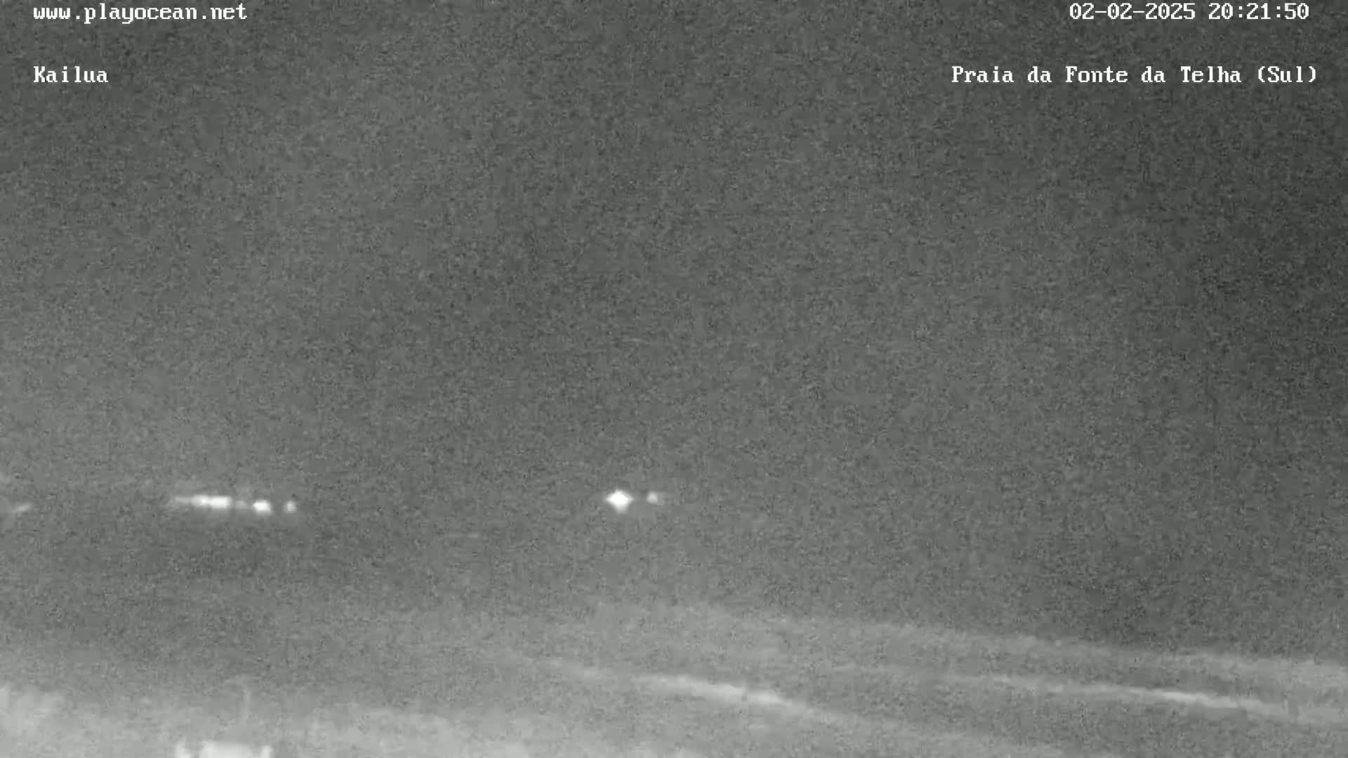 A nighttime, low-light image shows a dark, flat landscape with a few faint lights in the distance.