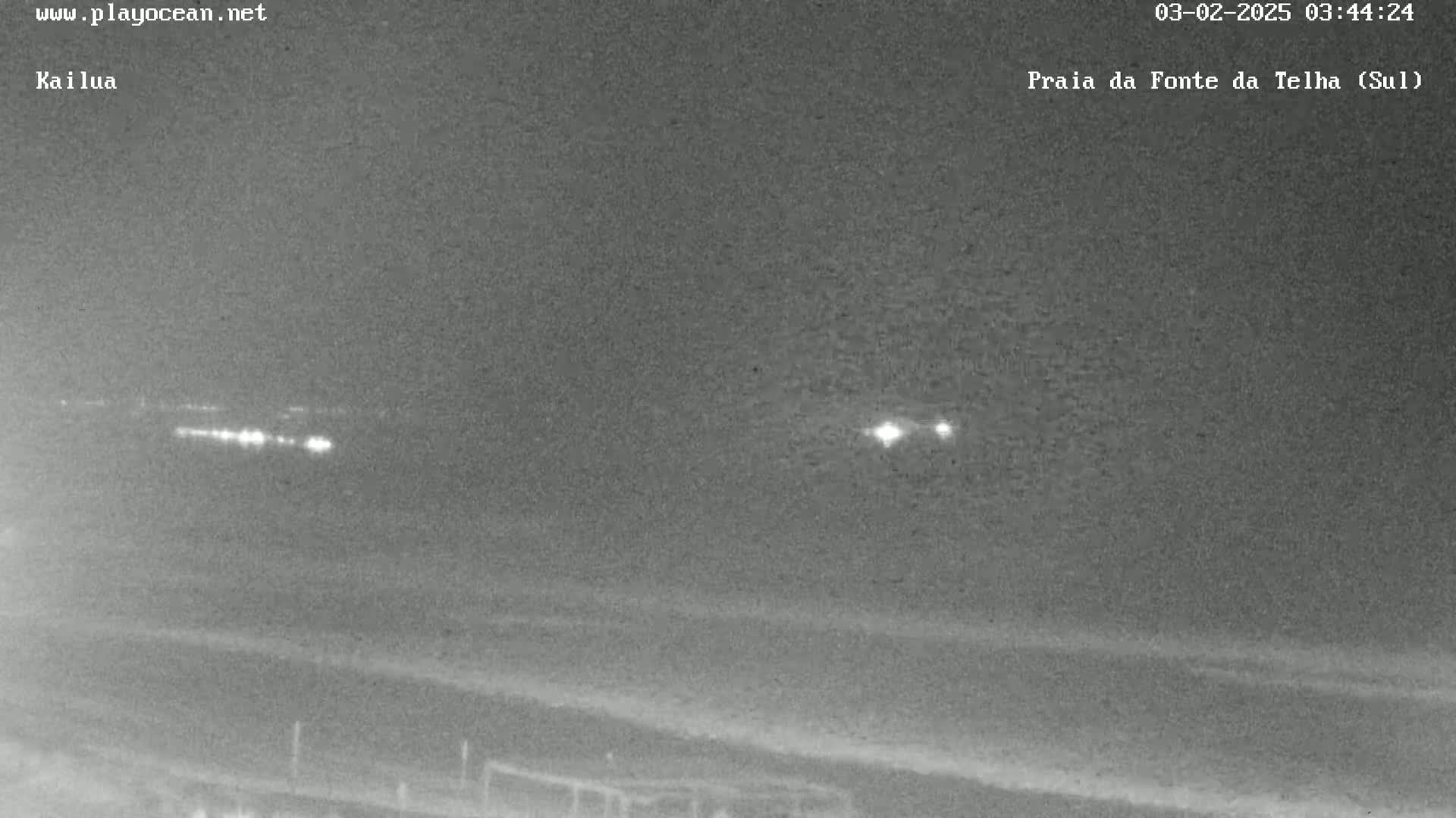A nighttime, low-light image shows a dark beach and a distant line of lights.
