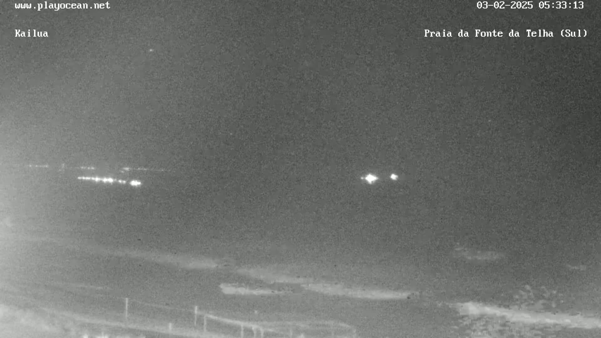 A nighttime, low-light view of a beach with distant lights visible on the horizon.