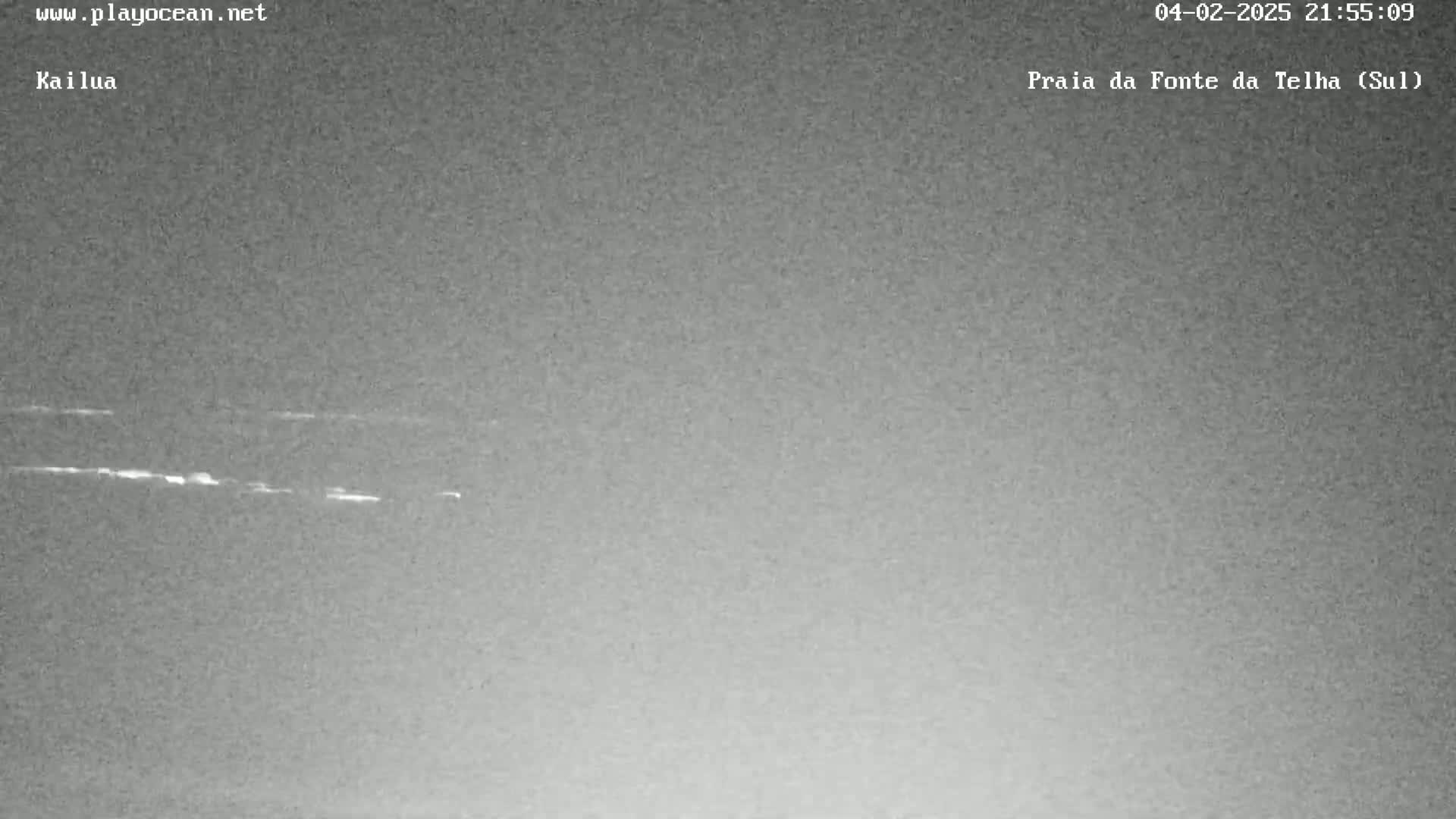 A low-light nighttime image shows a dark gray ocean with faint white lines near the horizon.