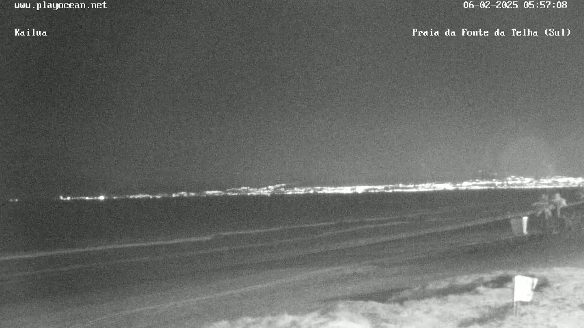 A nighttime view of a dark beach with a distant city skyline illuminated by lights.