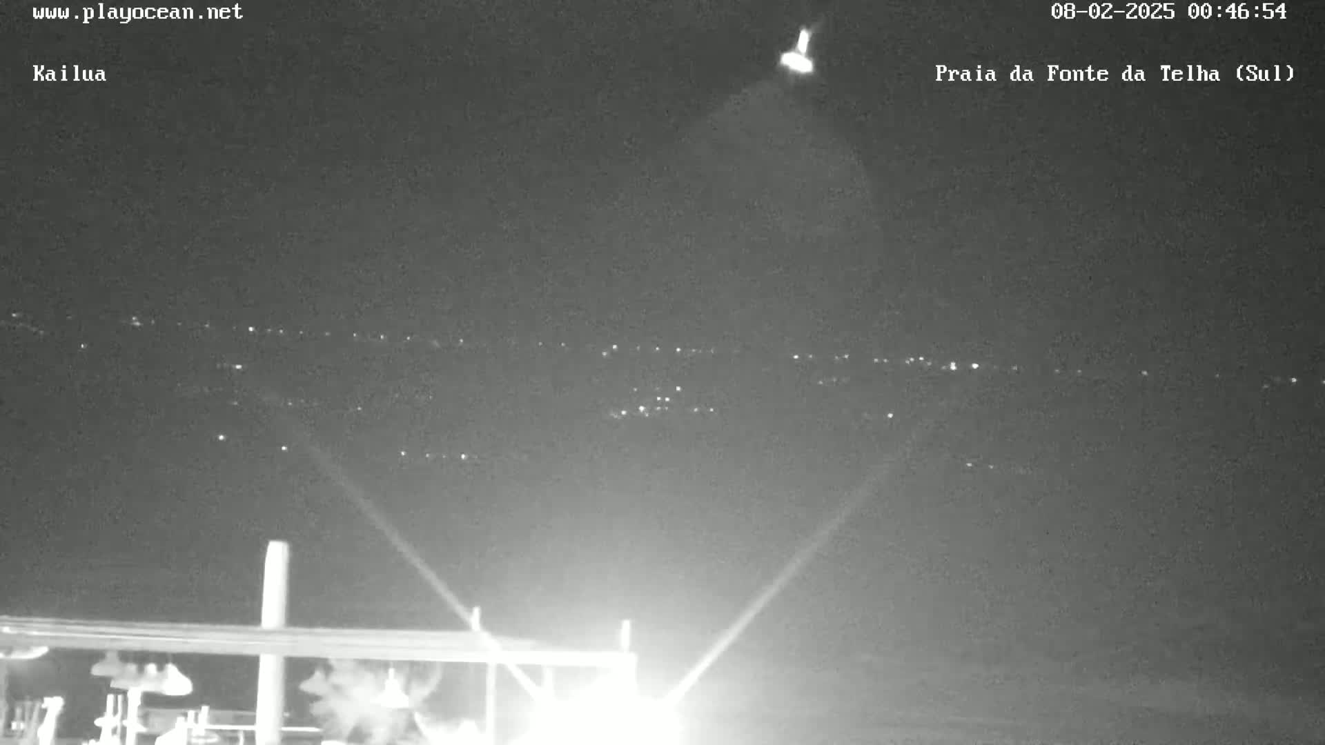 A nighttime view shows a distant line of lights on a dark horizon, illuminated by bright lights in the foreground.