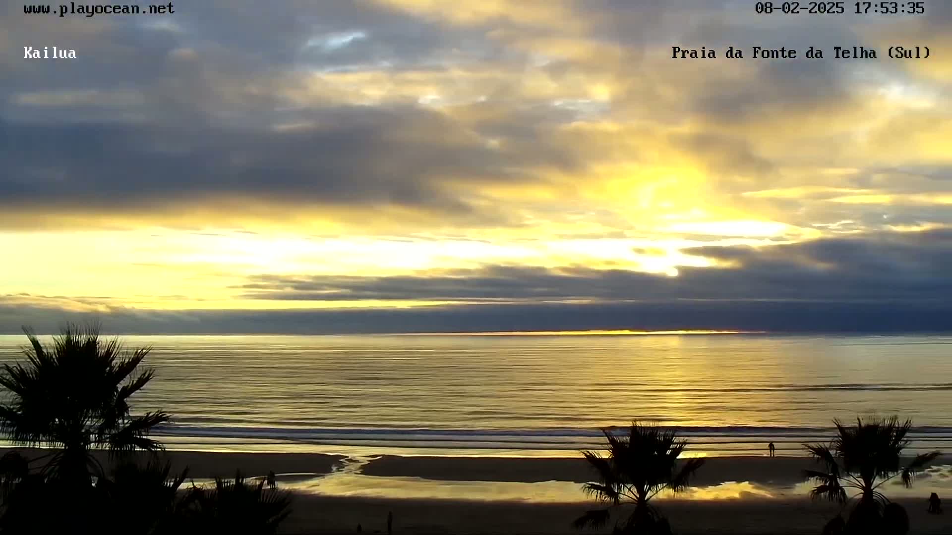 A beach scene at sunset with a mostly cloudy sky showing streaks of yellow and gold light over a calm ocean.