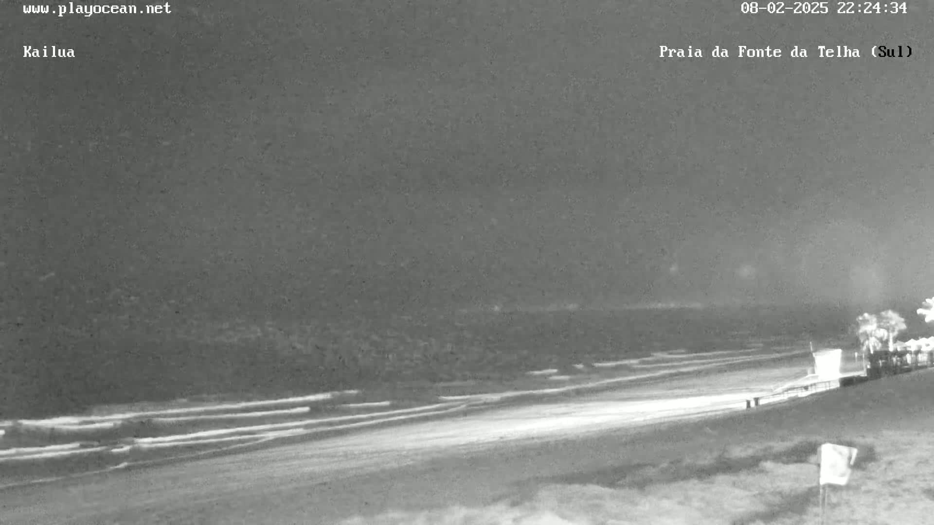 A nighttime, low-light view of a beach with gentle waves lapping the shore.