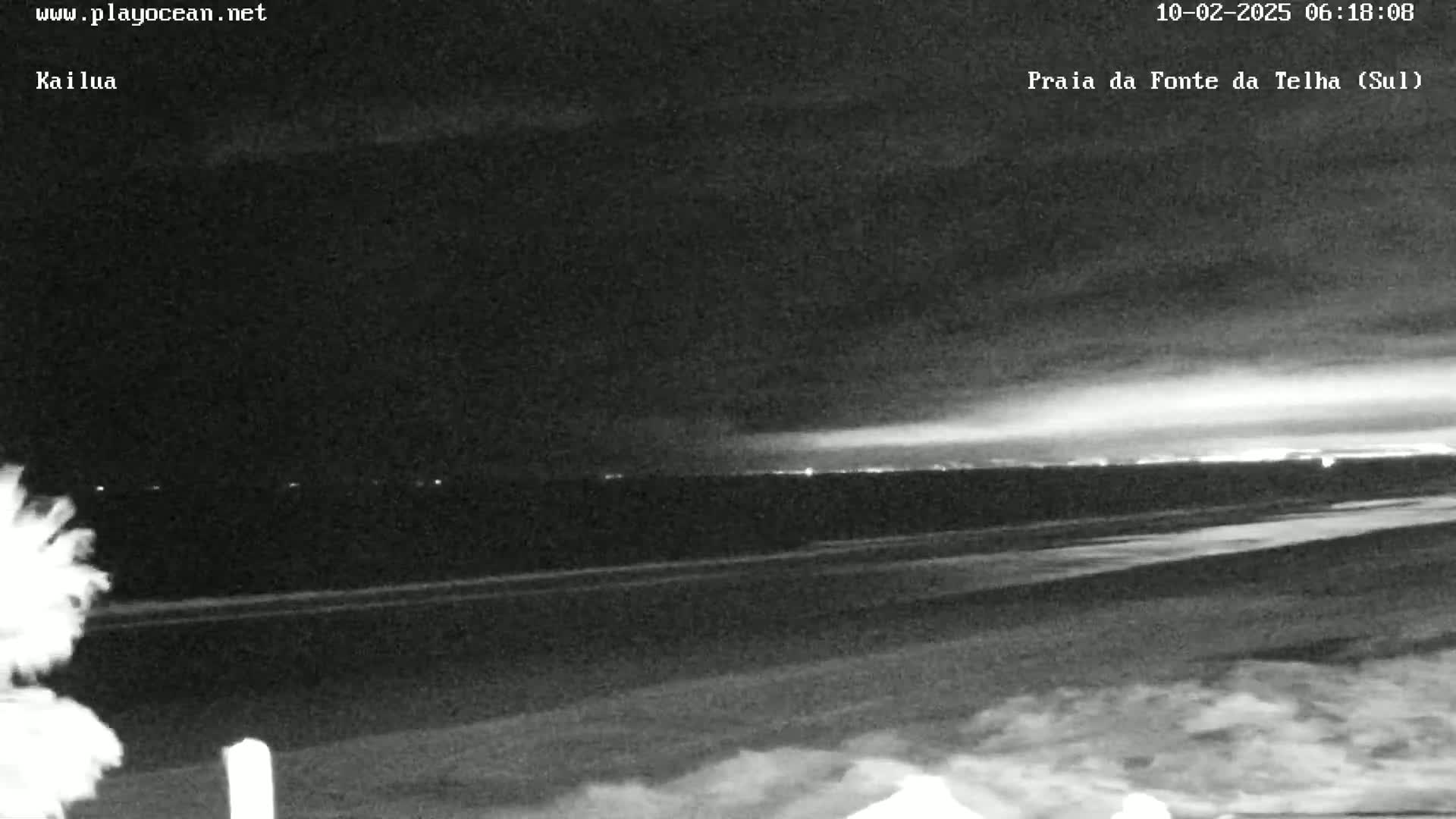 A nighttime, overcast view of a beach with a distant horizon showing city lights.