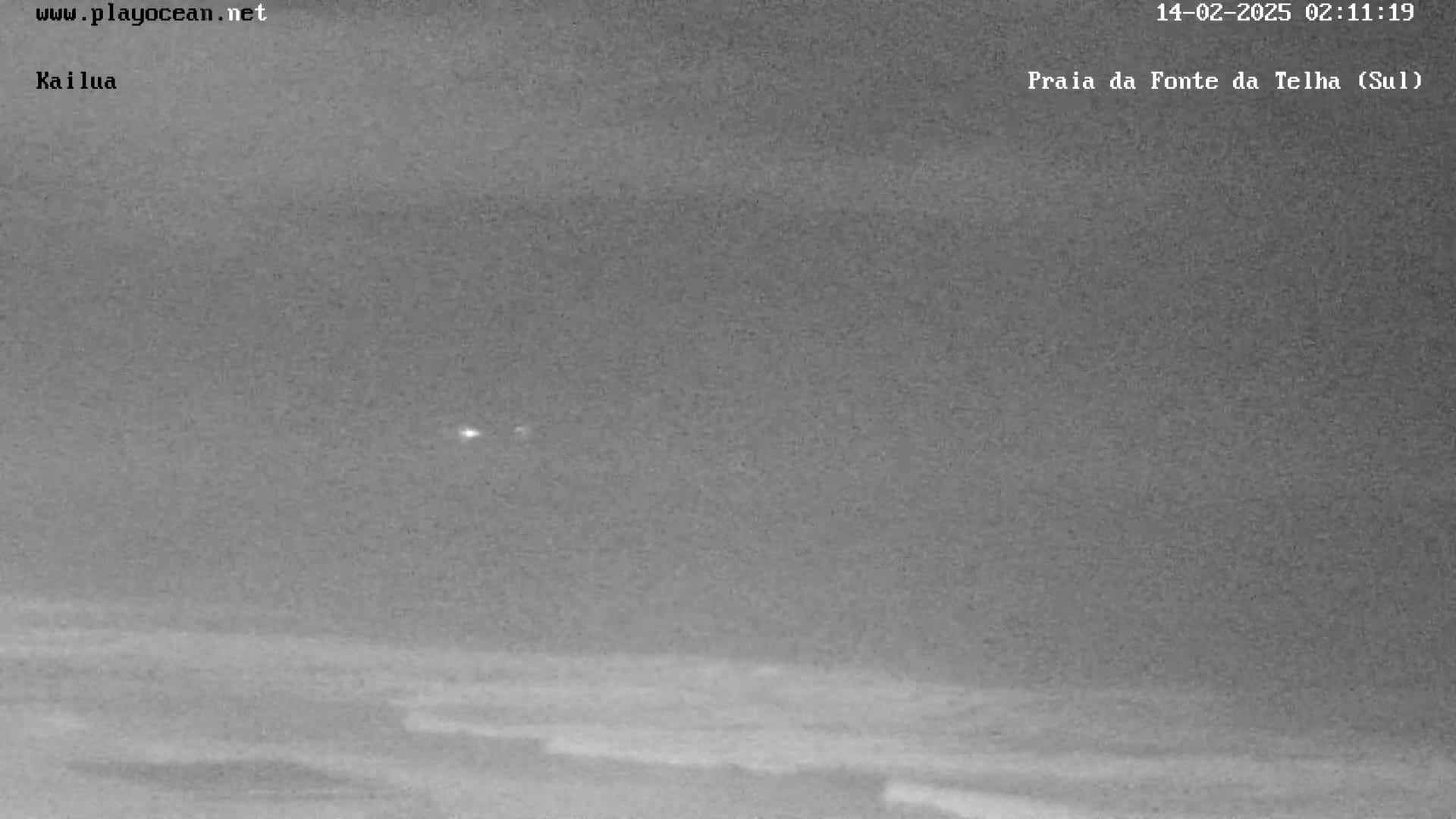 A nighttime, overcast view shows a dark ocean with small waves gently rolling onto a beach.