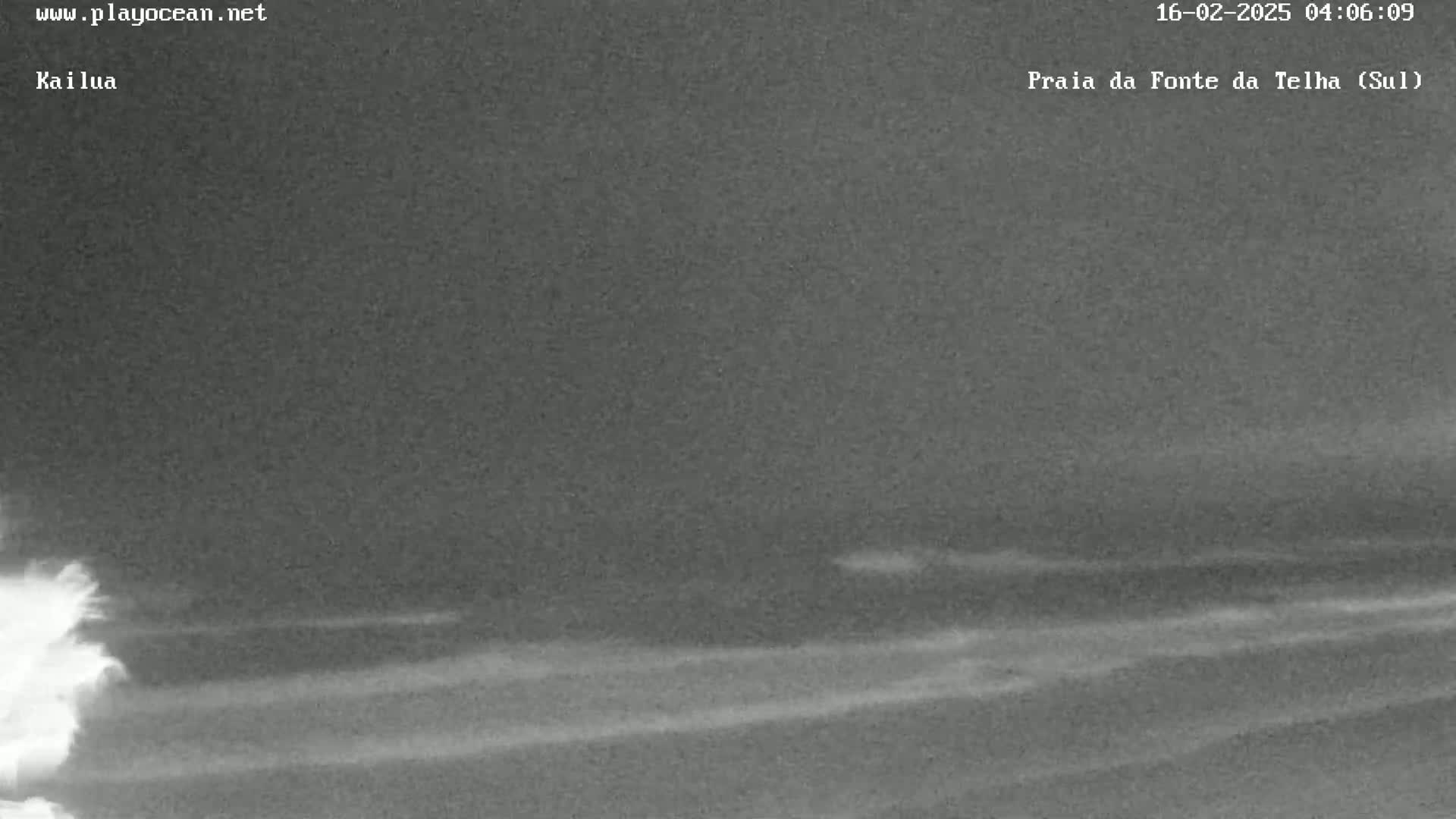 A nighttime, low-light image shows a dark ocean with small waves under a cloudy sky.