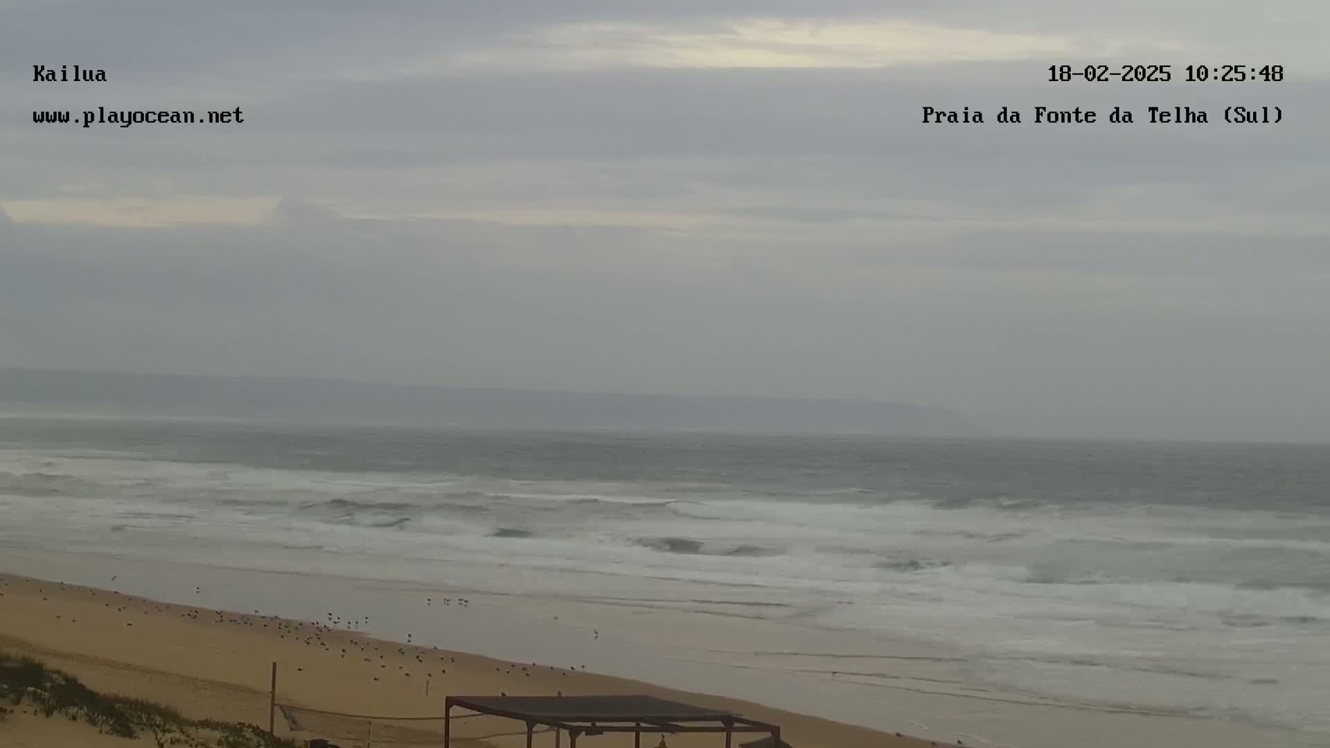 A sandy beach with gentle waves under an overcast sky.