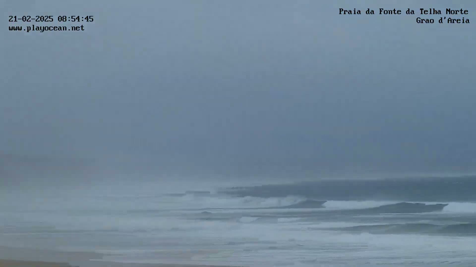A hazy, overcast day shows a beach with moderate waves breaking in the ocean.