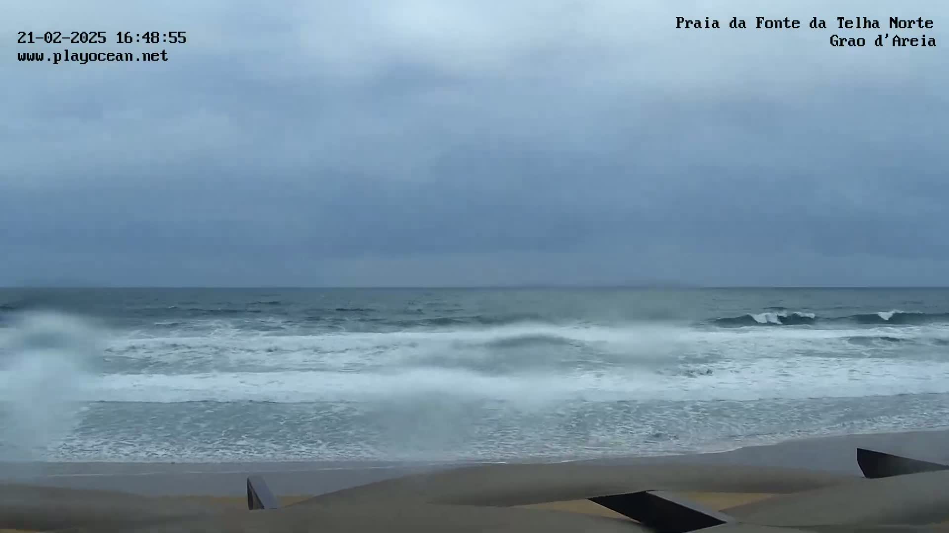 A sandy beach with choppy waves under an overcast sky.