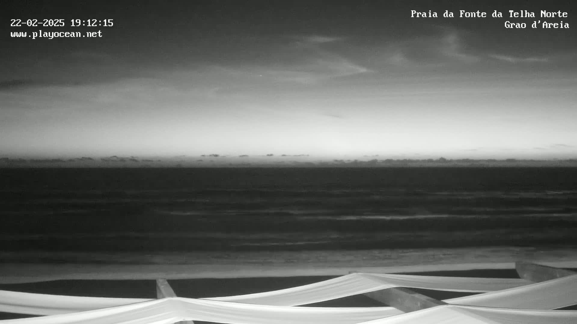 A grayscale image shows a dark, overcast sky over a wavy ocean at twilight, with a section of what appears to be beach furniture in the foreground.