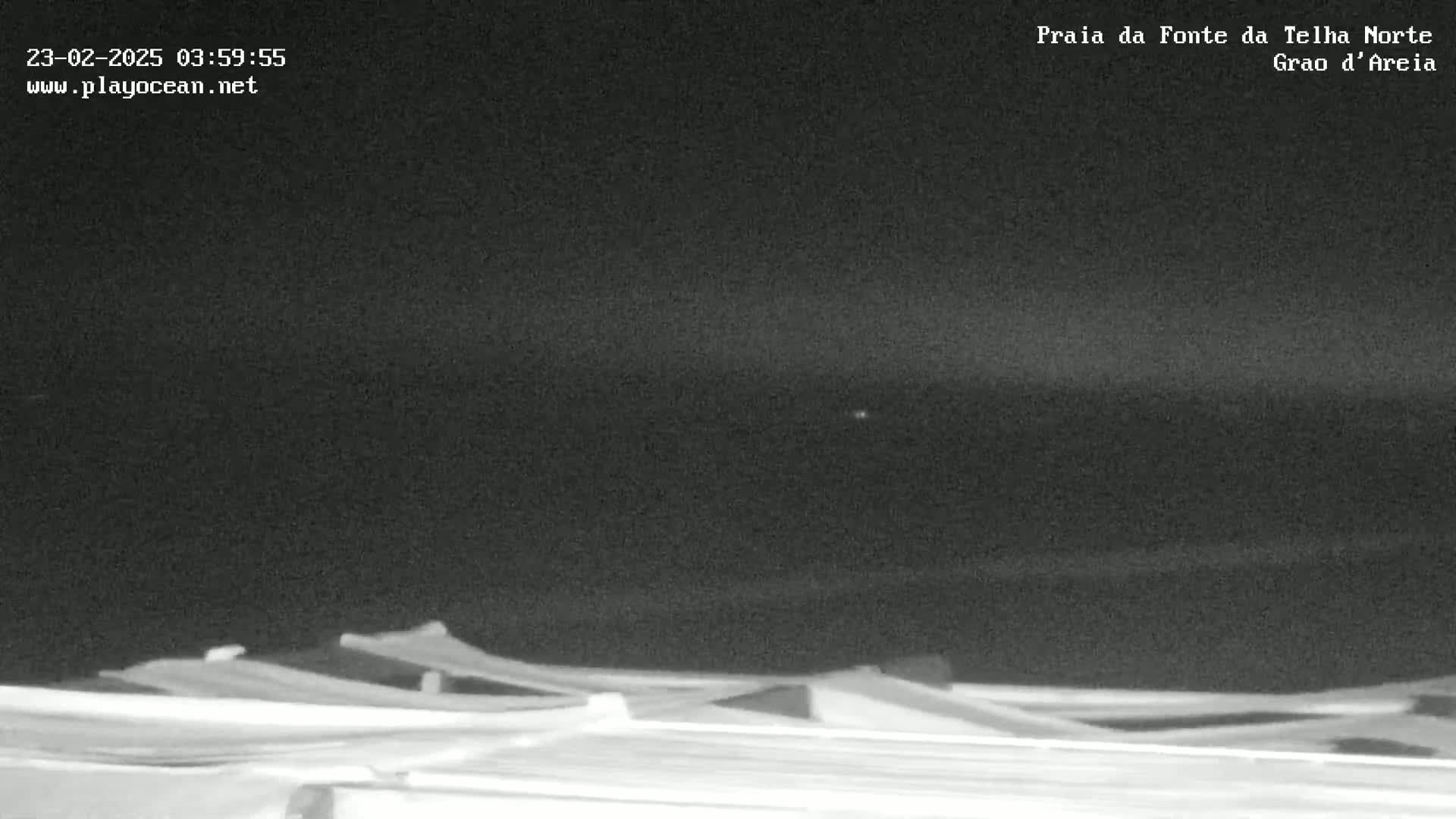 A nighttime, low-light image shows a dark ocean meeting a dark sky, with the tops of several structures visible in the foreground.