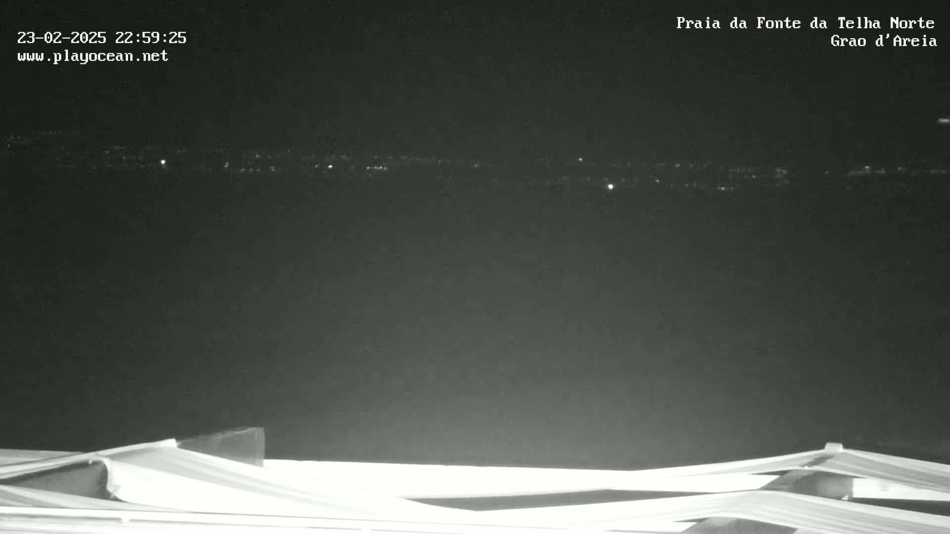 A nighttime, long-distance view shows a dark horizon with distant city lights, and in the foreground is a section of a white structure.