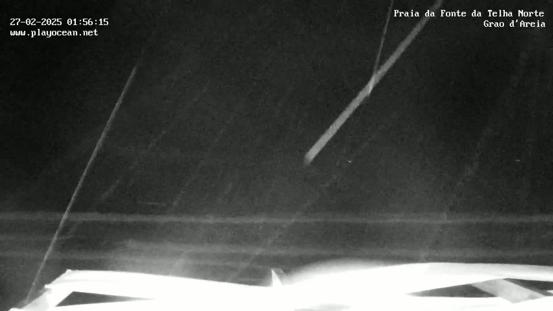 A nighttime, low-light image shows a dark, possibly sandy, landscape under a mostly clear sky with a bright streak possibly from a meteor.