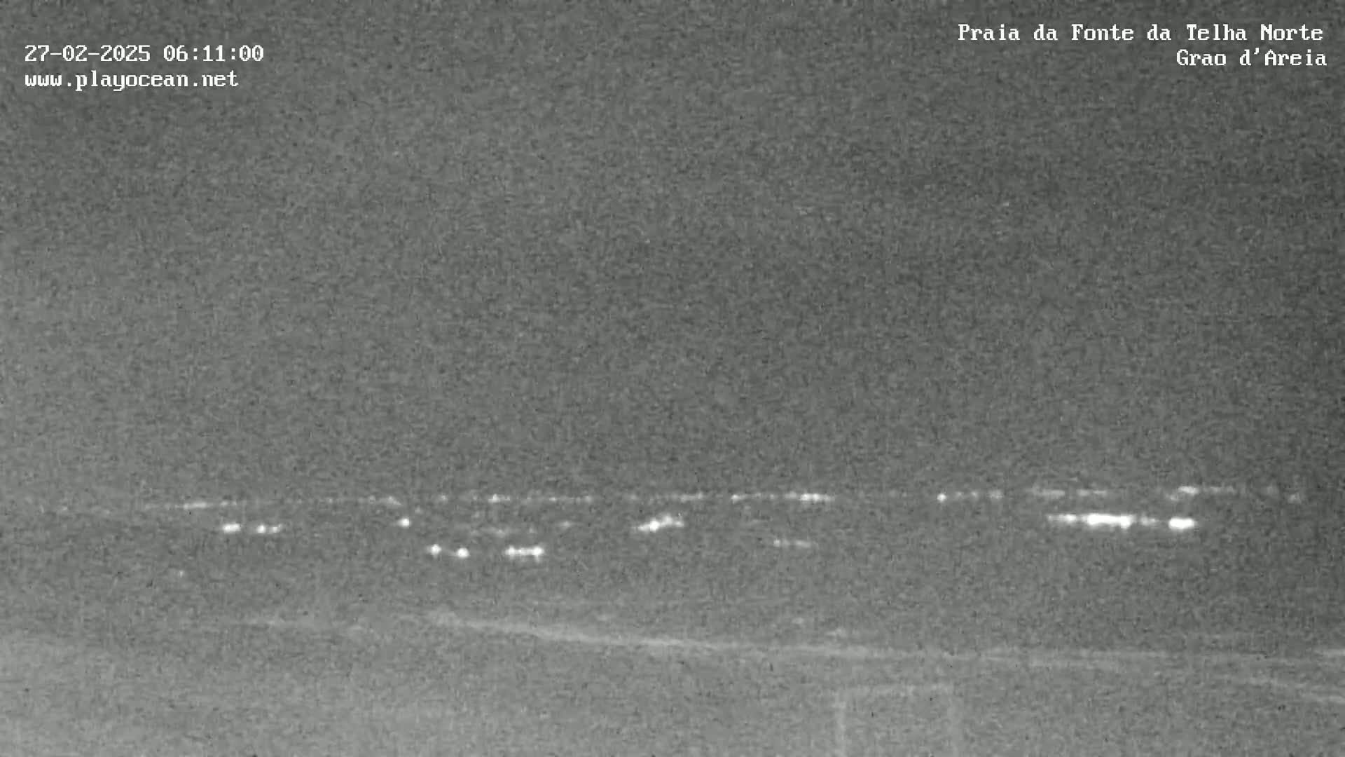 A low-light, nighttime image shows a distant line of lights on the horizon.