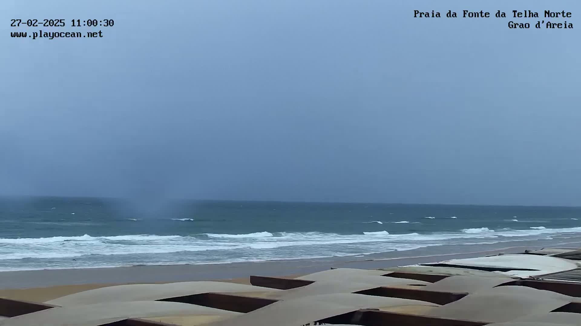 A wide shot shows a beach with moderate waves under an overcast sky.