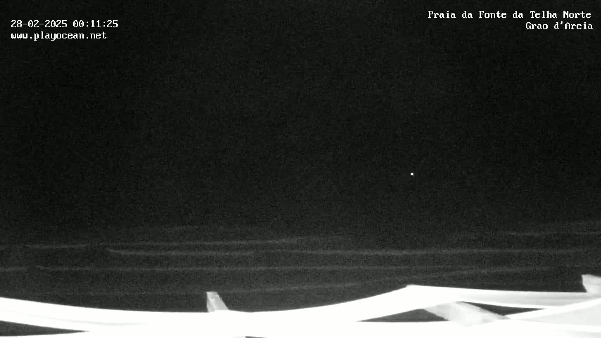 A nighttime, low-light image shows dark ocean waves lapping at the bottom of a beach structure under a clear, dark sky.