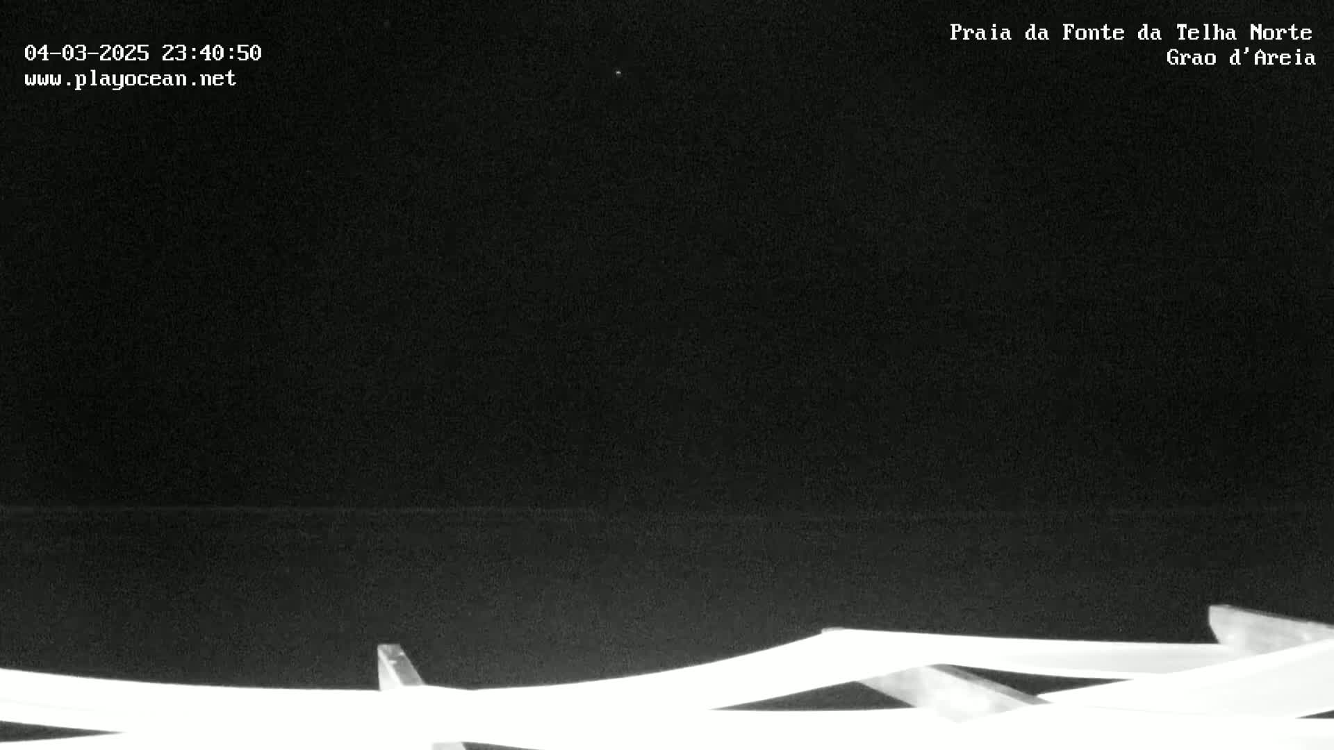 A nighttime, low-light view of a dark body of water with what appears to be a white structure, possibly beach furniture, in the bottom of the frame.