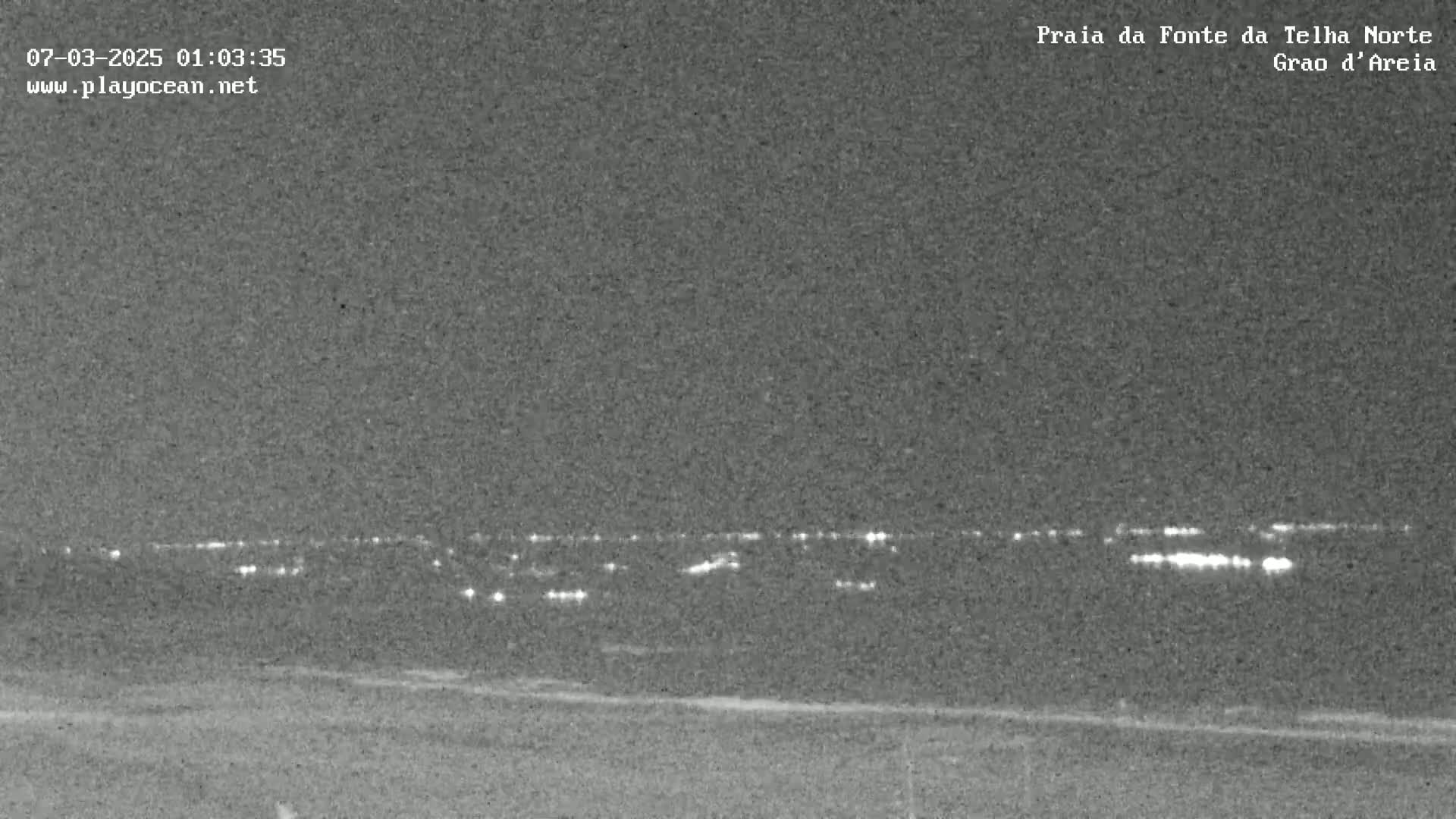 A nighttime, low-light image shows a distant line of lights on the horizon.