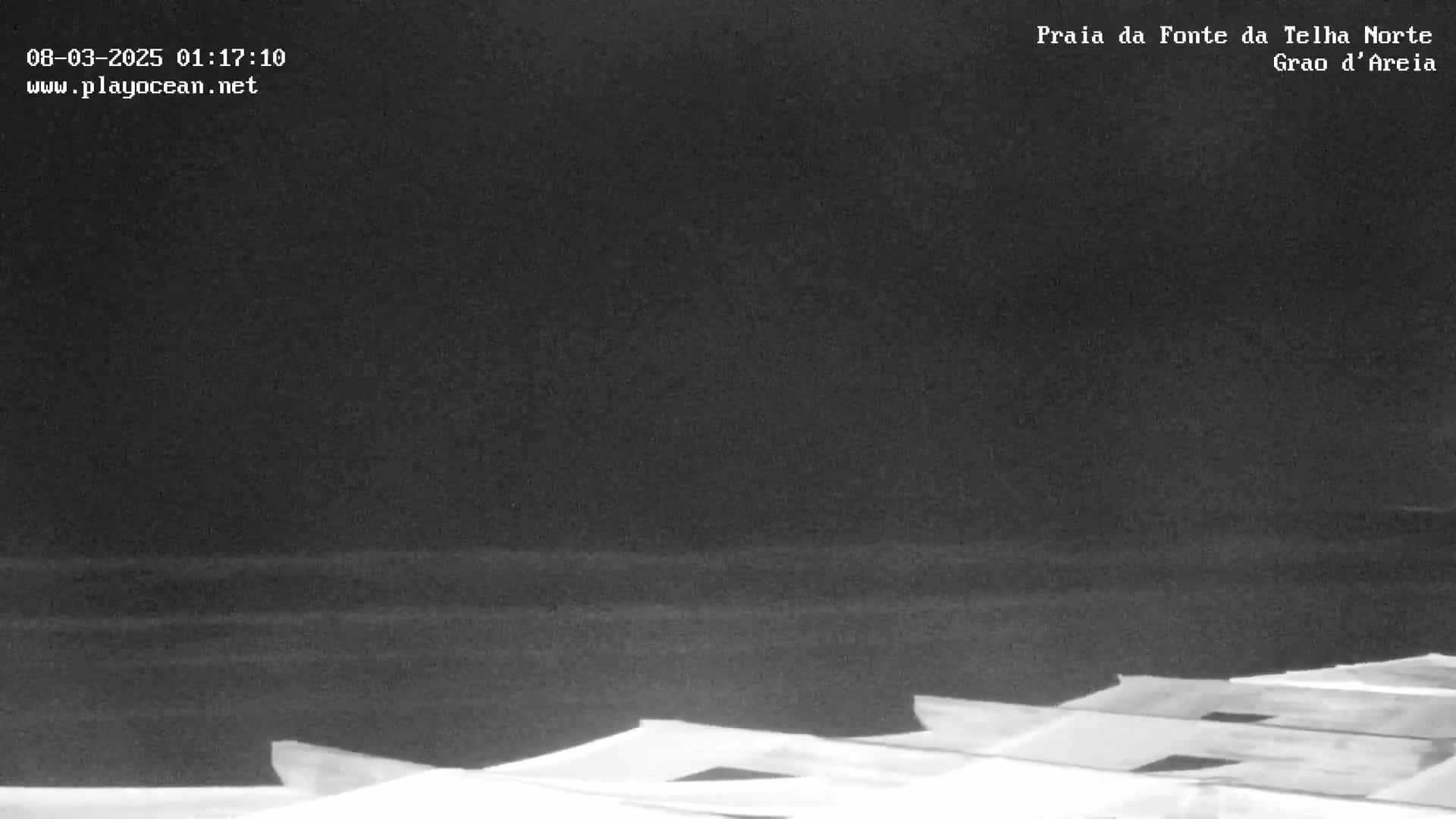 A nighttime, low-light view of a dark beach and the tops of structures in the foreground.