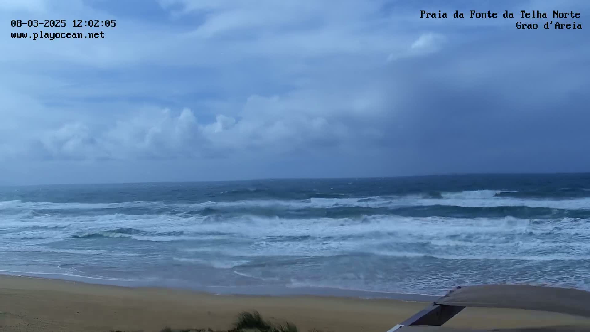 A partly cloudy sky overlooks a sandy beach with moderately rough ocean waves.