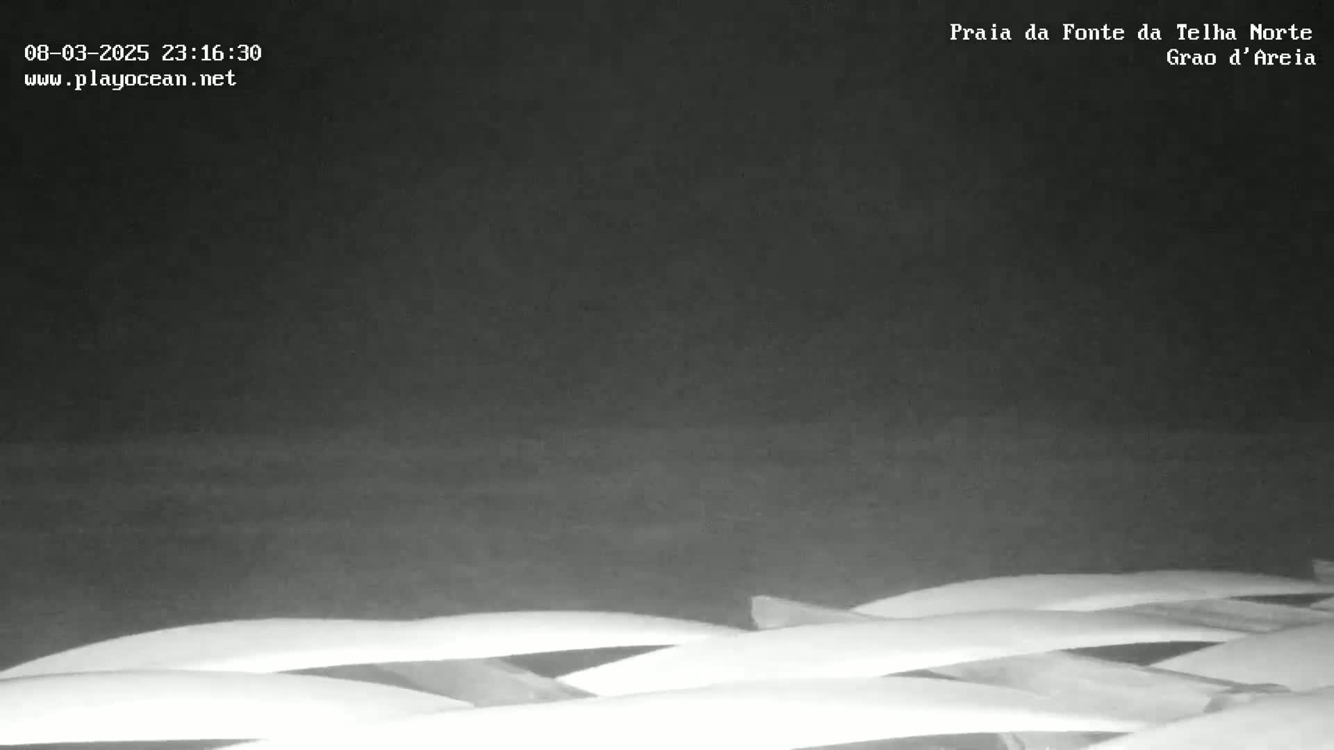 Under a dark night sky, several rows of white beach loungers are visible on a beach.
