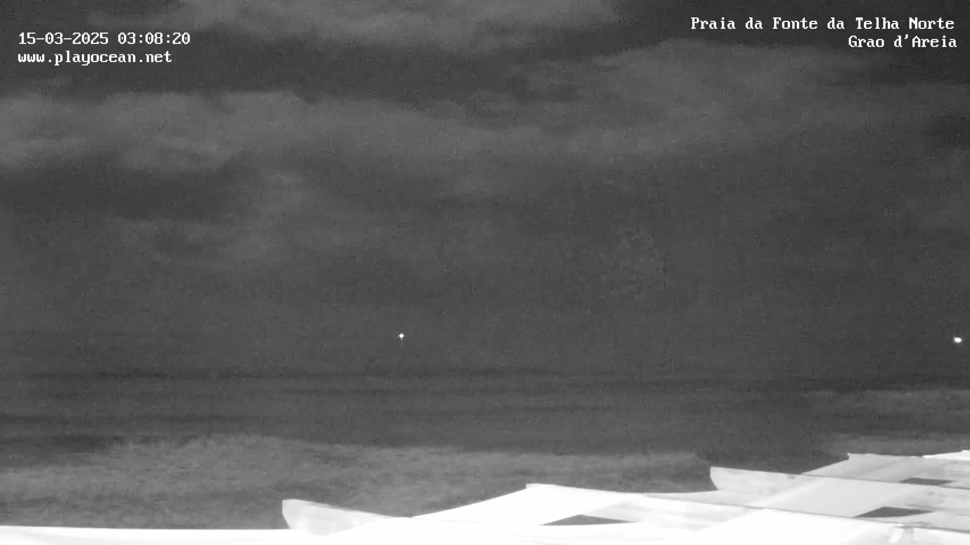A nighttime, overcast beach scene shows a dark ocean and several pale, flat objects in the bottom right corner.