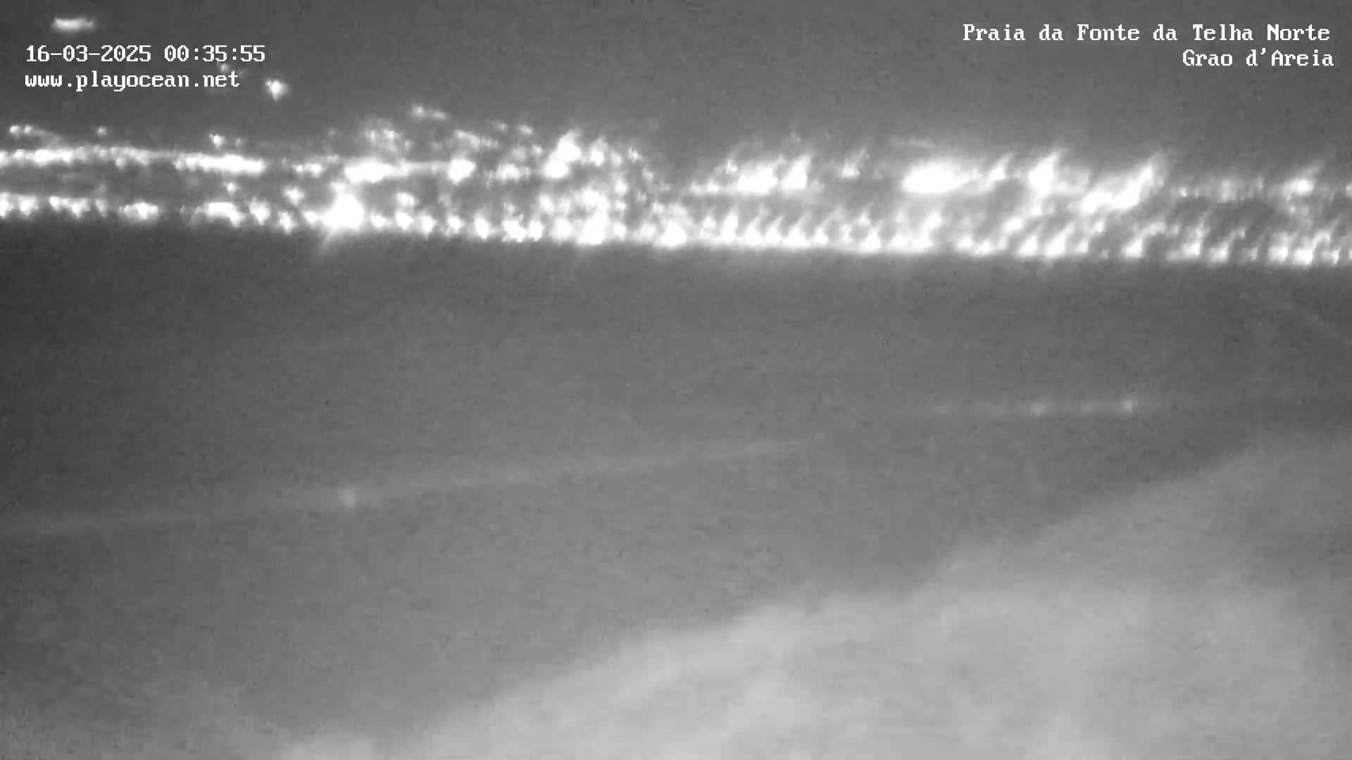 A nighttime, low-light image shows a distant line of lights, possibly buildings or a town, on a dark, hazy horizon.