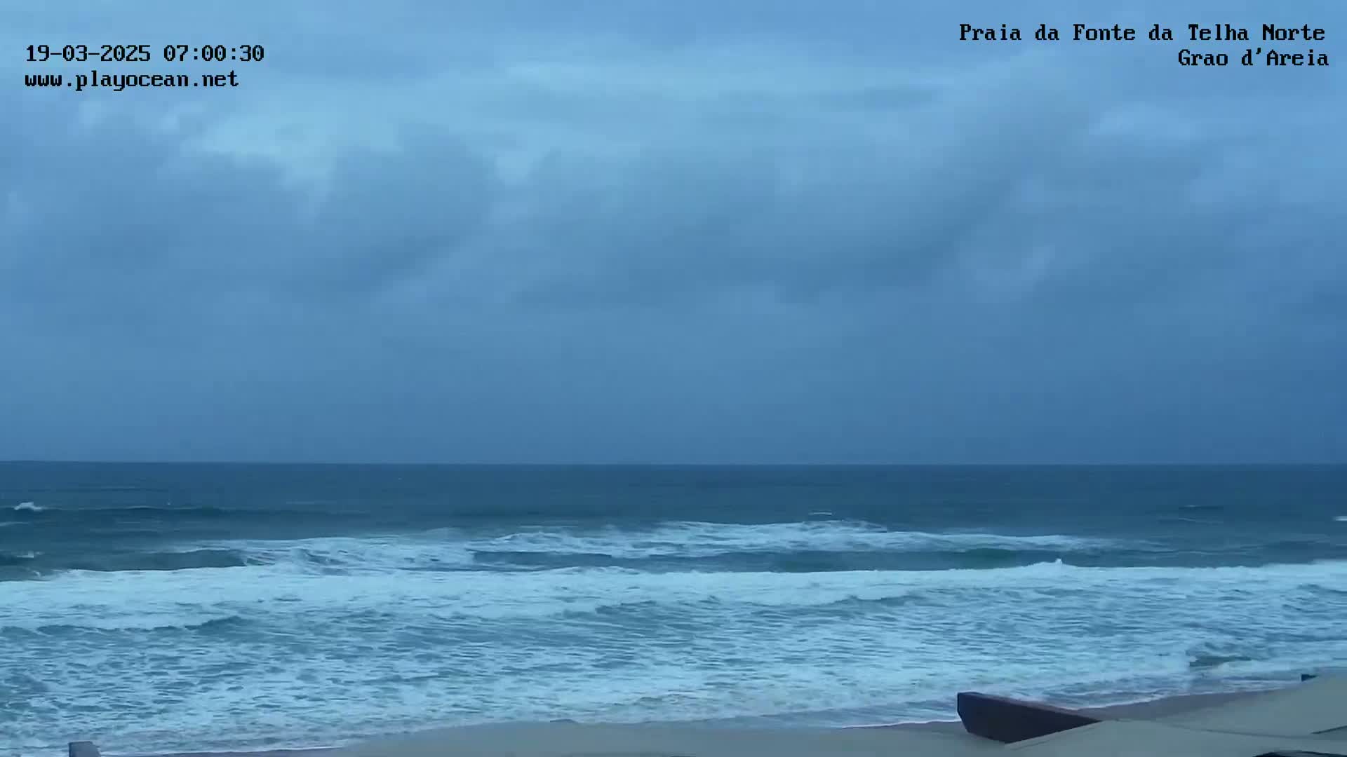 An overcast sky looms over a beach with moderate waves rolling onto the shore.