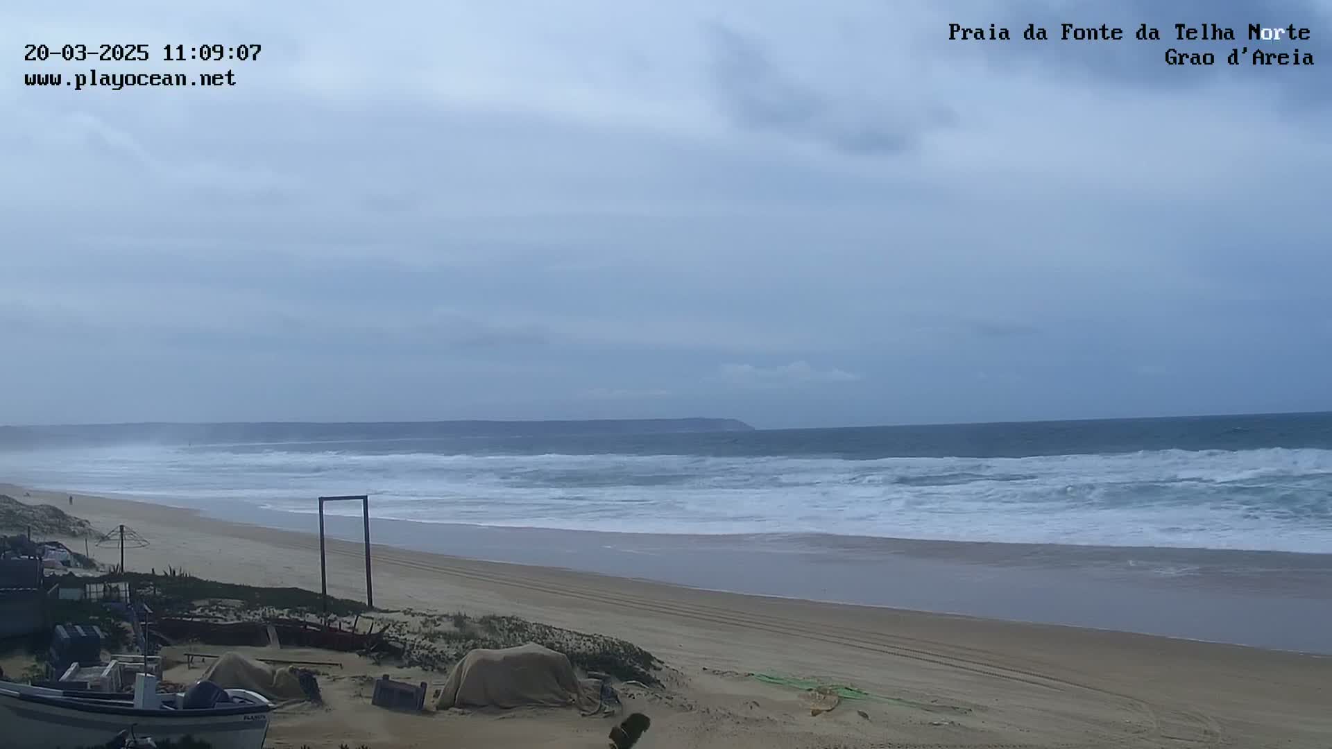 A wide sandy beach stretches to a wavy ocean under an overcast sky.