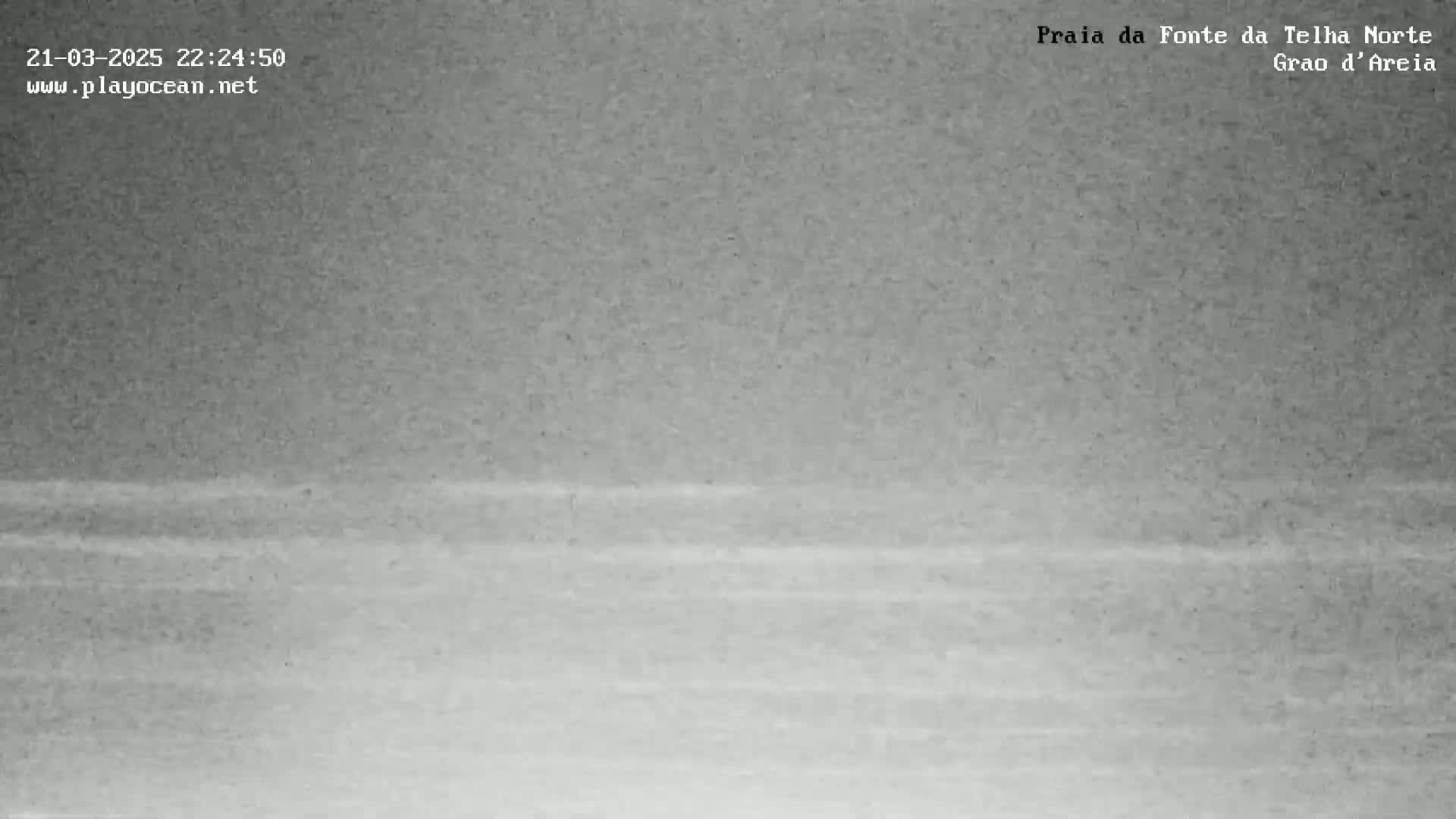 A grainy, low-light image shows a dark body of water with subtle wave patterns under a dark, likely nighttime sky.