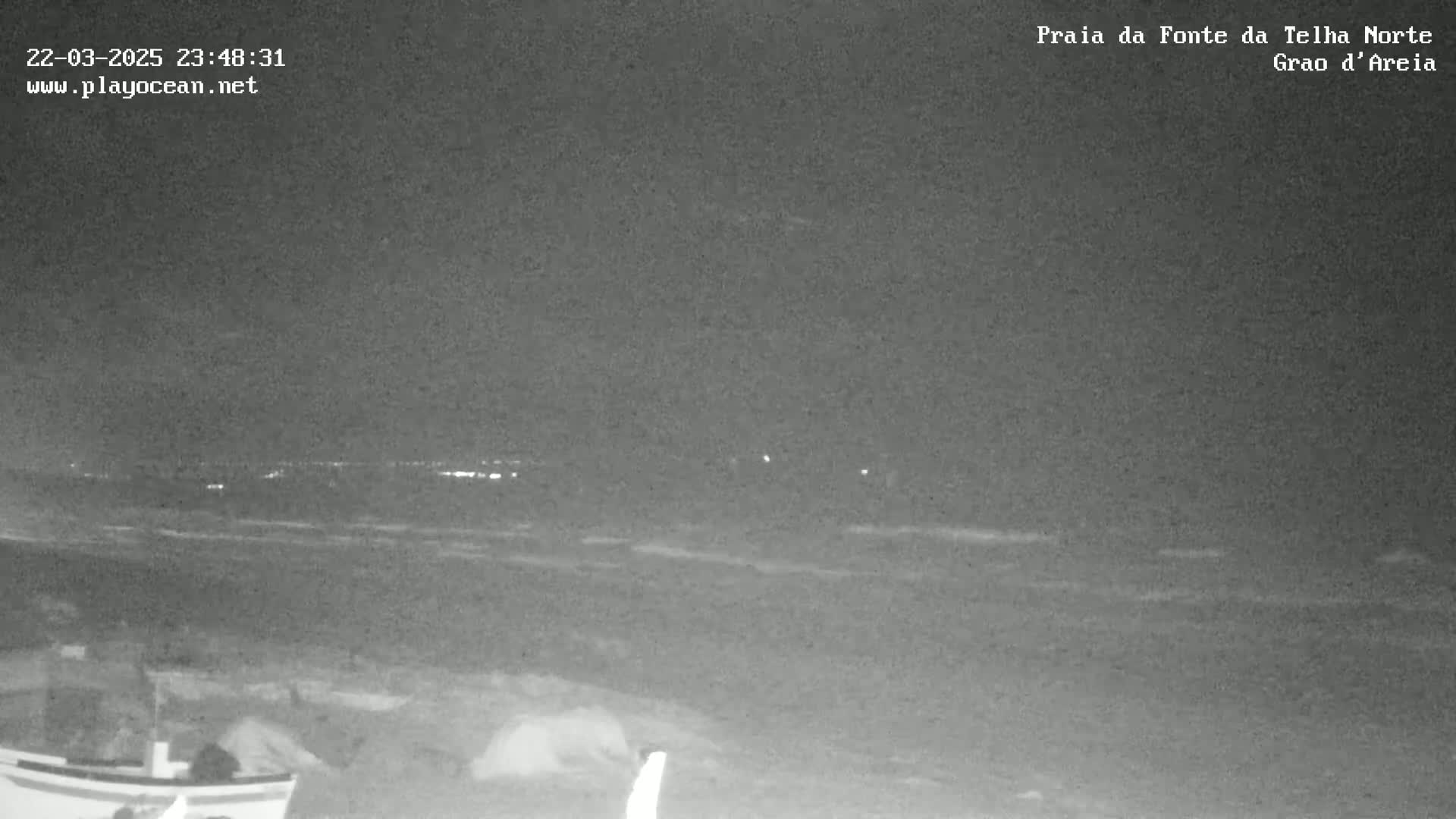 A nighttime view of a dark beach with a choppy ocean under a clear sky.