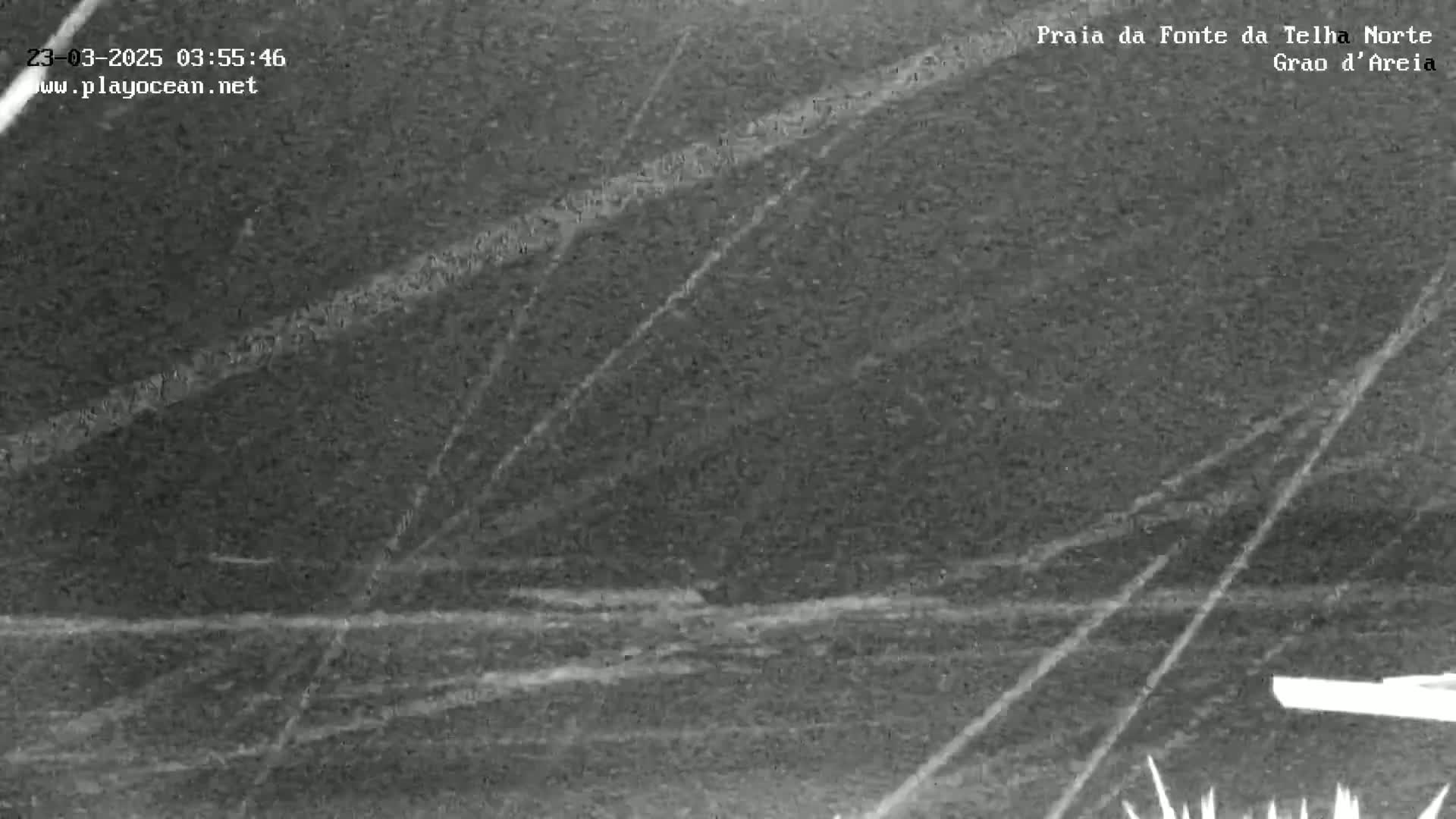A nighttime, low-light image shows a dark beach with faint, diagonal lines across it, possibly from rain or waves.
