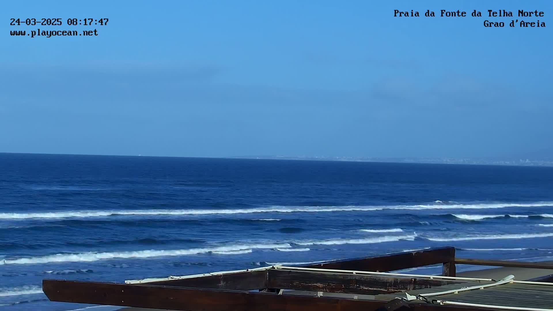 A dark wooden structure overlooks a blue ocean with small waves under a clear blue sky.