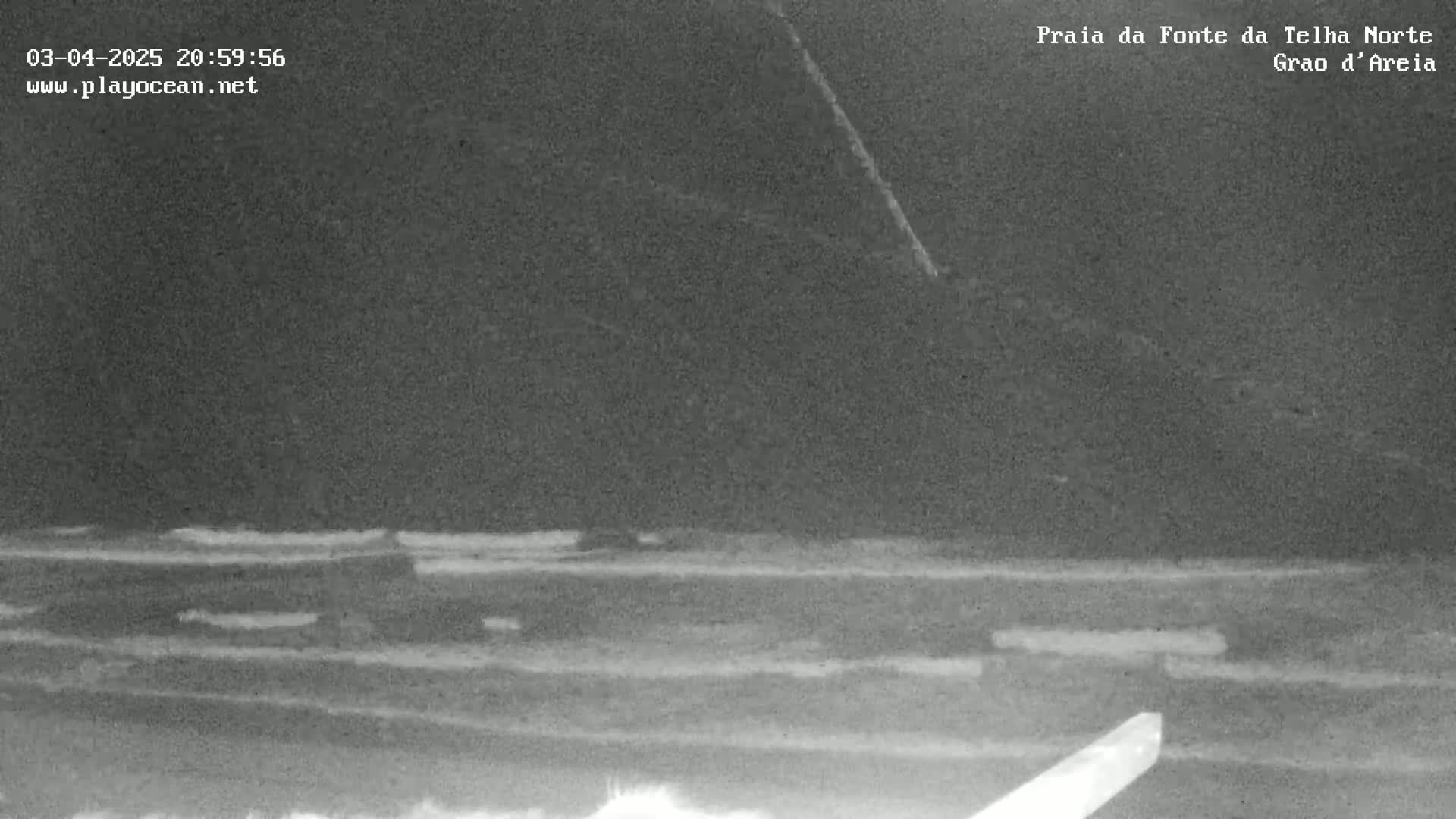 A nighttime, low-light image shows dark sand and ocean waves, possibly at a beach.