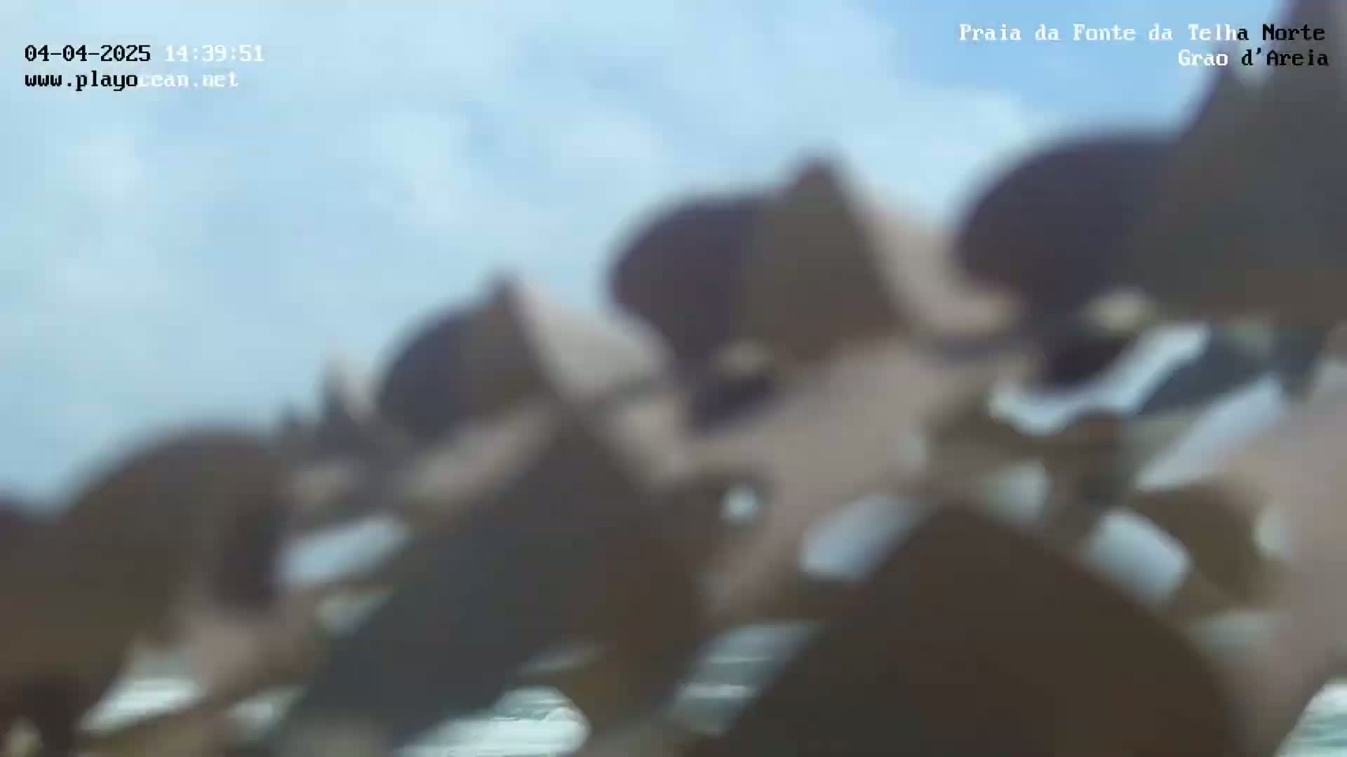 A blurry image shows a beach scene under a mostly clear sky.