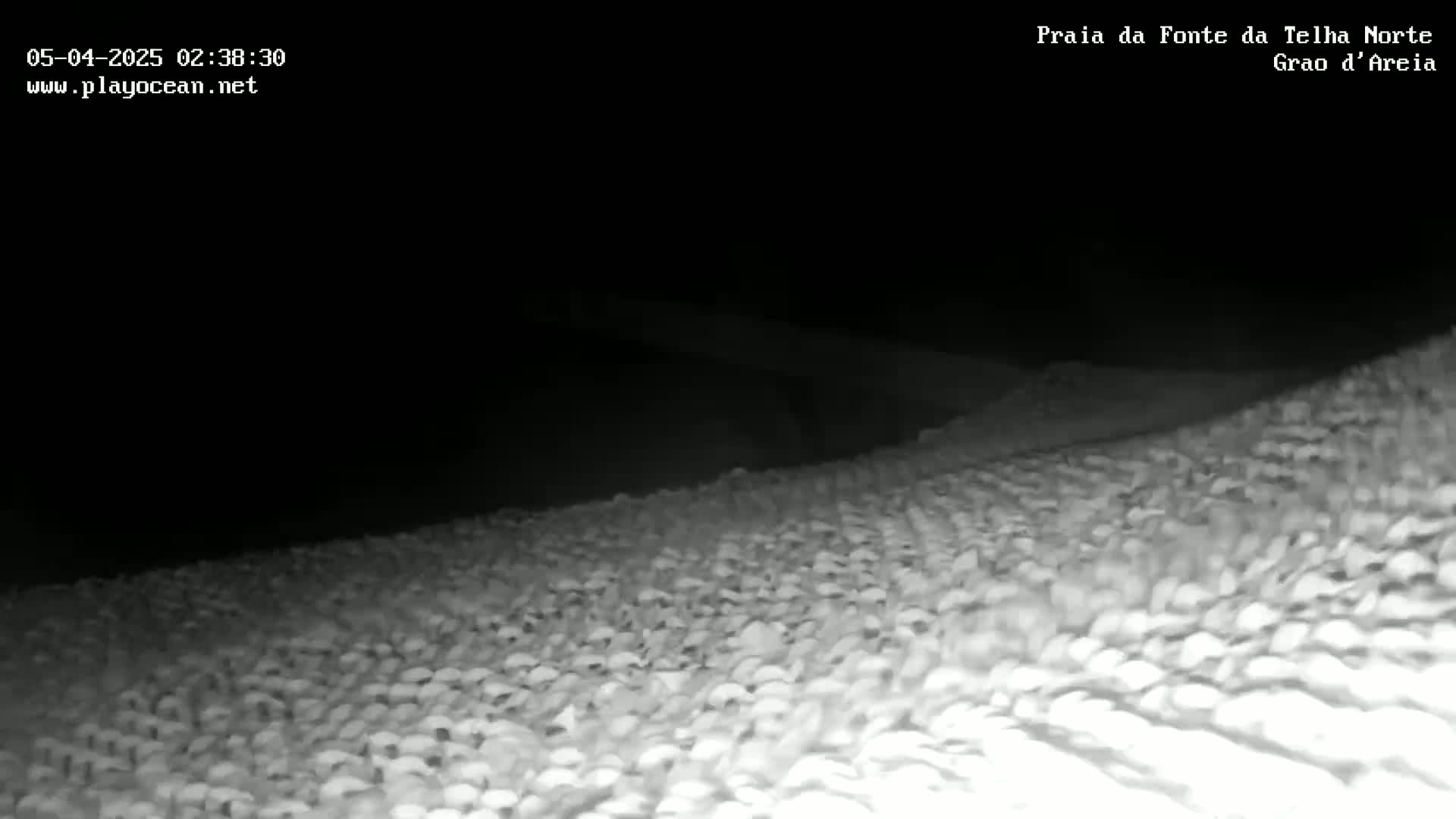 A nighttime, low-angle view shows a sandy beach extending into the darkness.