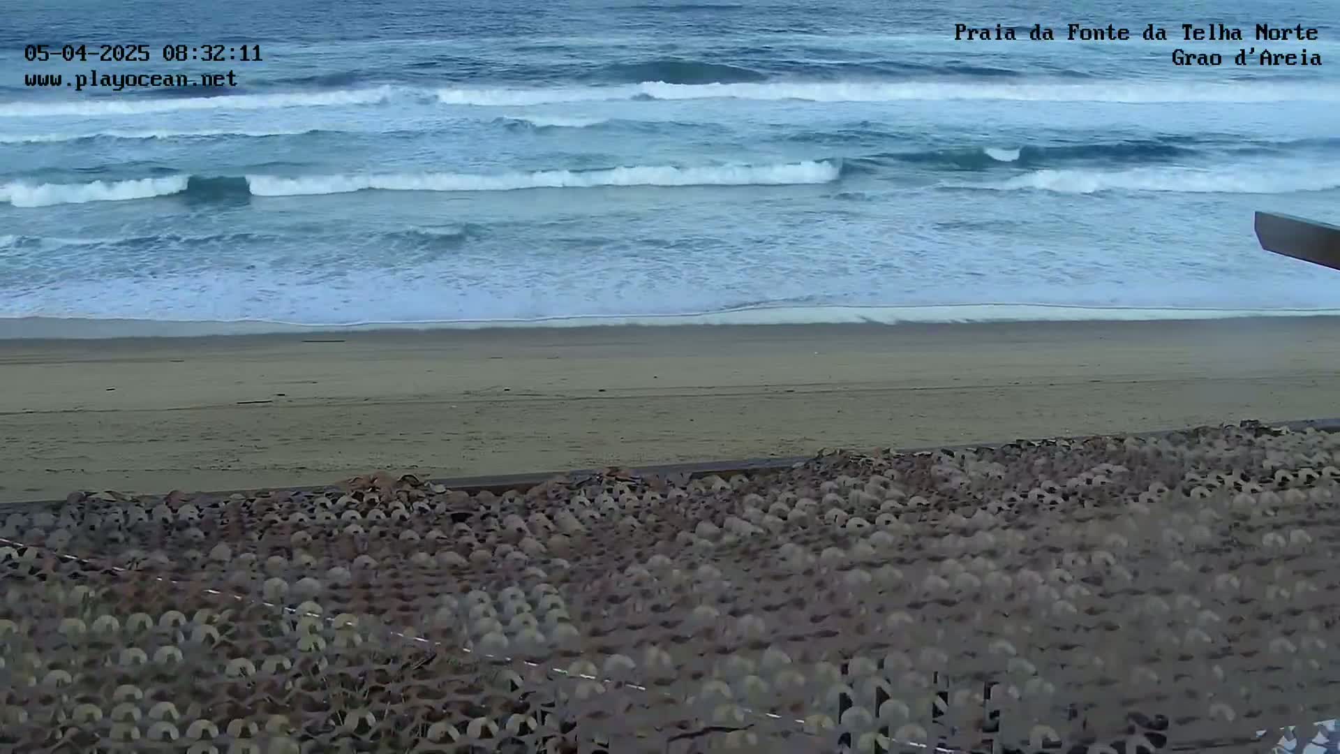 Ocean waves roll onto a sandy beach, where a large, textured structure sits in the foreground.