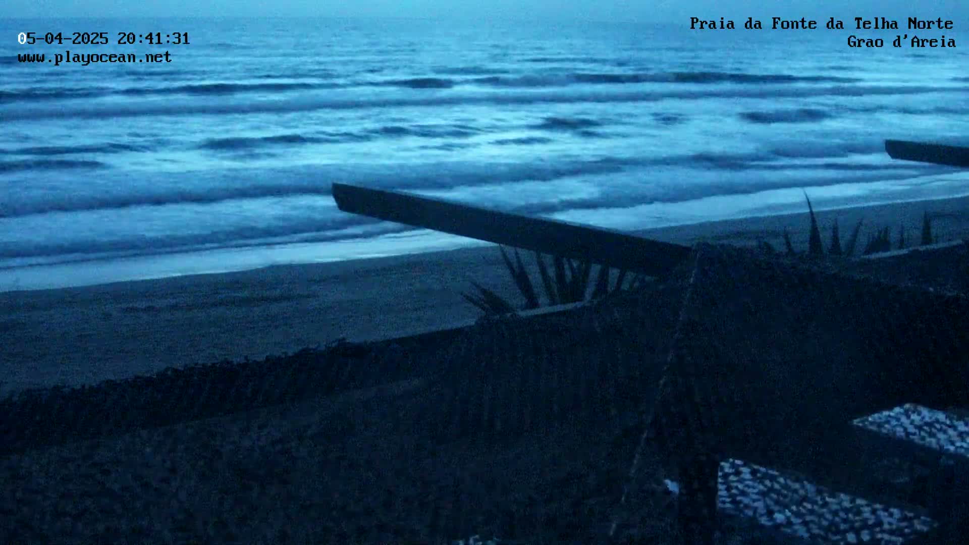 A dark, sandy beach is partially visible under an evening sky, with gentle waves rolling onto the shore.