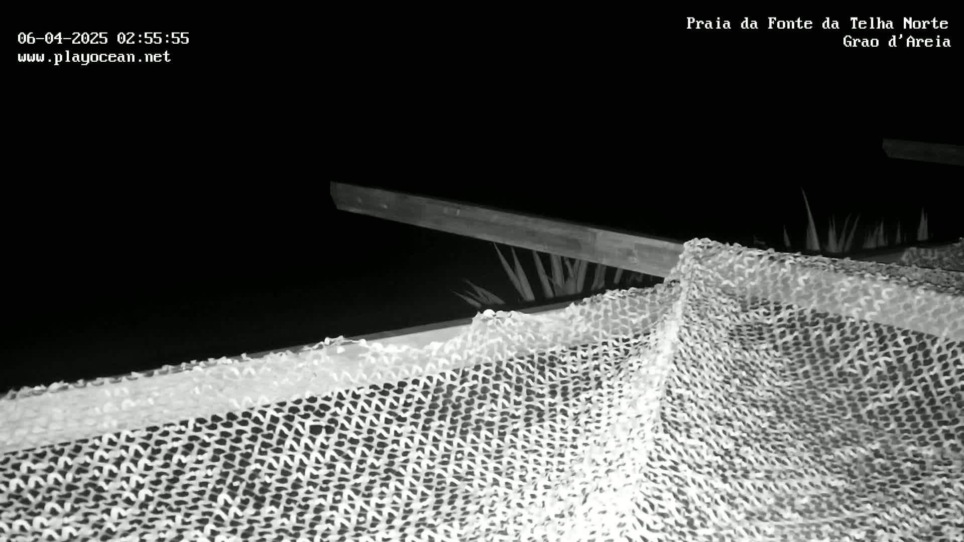 At night, a section of netting drapes over a wooden structure, partially obscuring some vegetation.