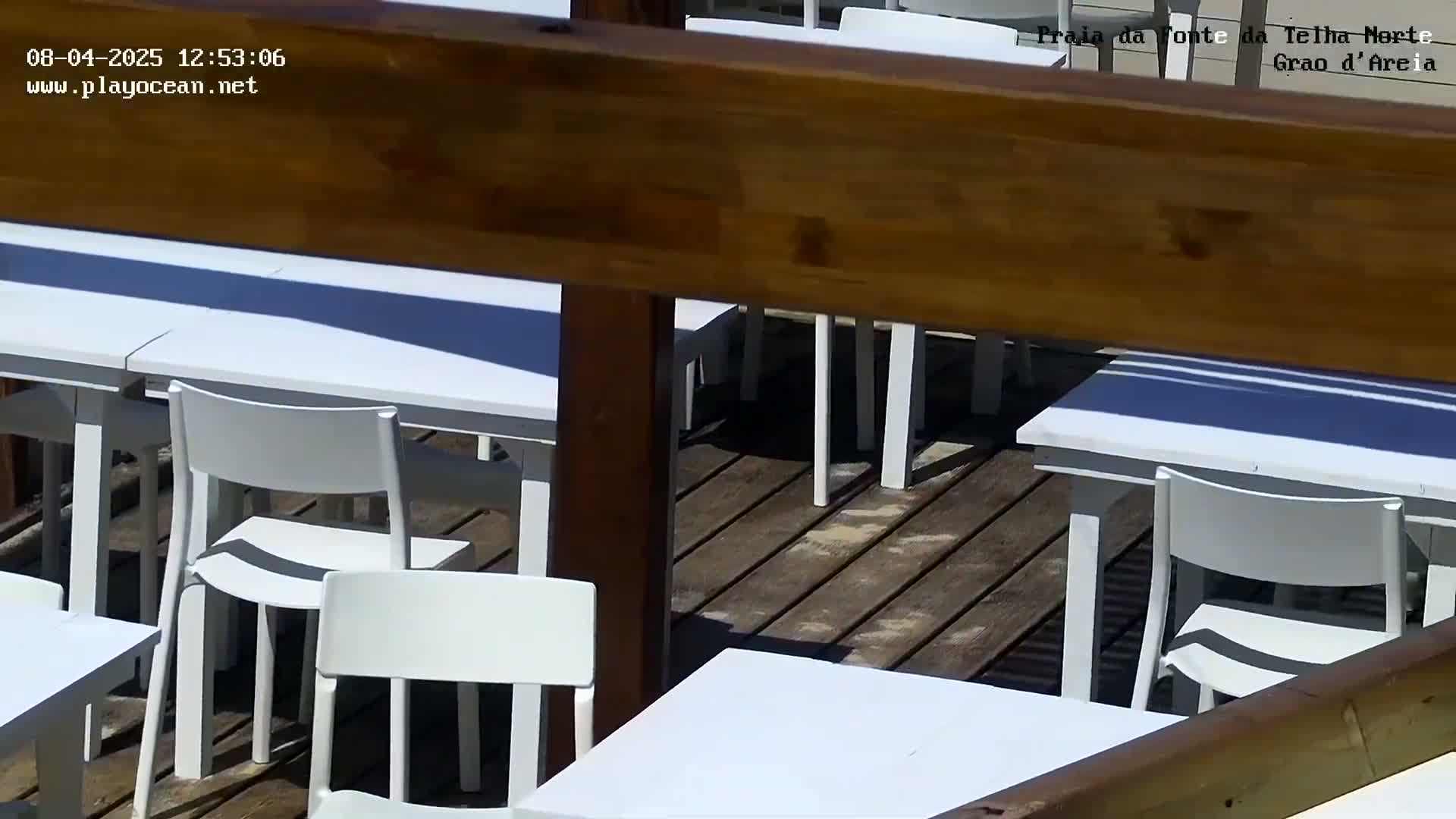 A sunny outdoor patio with white tables and chairs on a wooden deck.