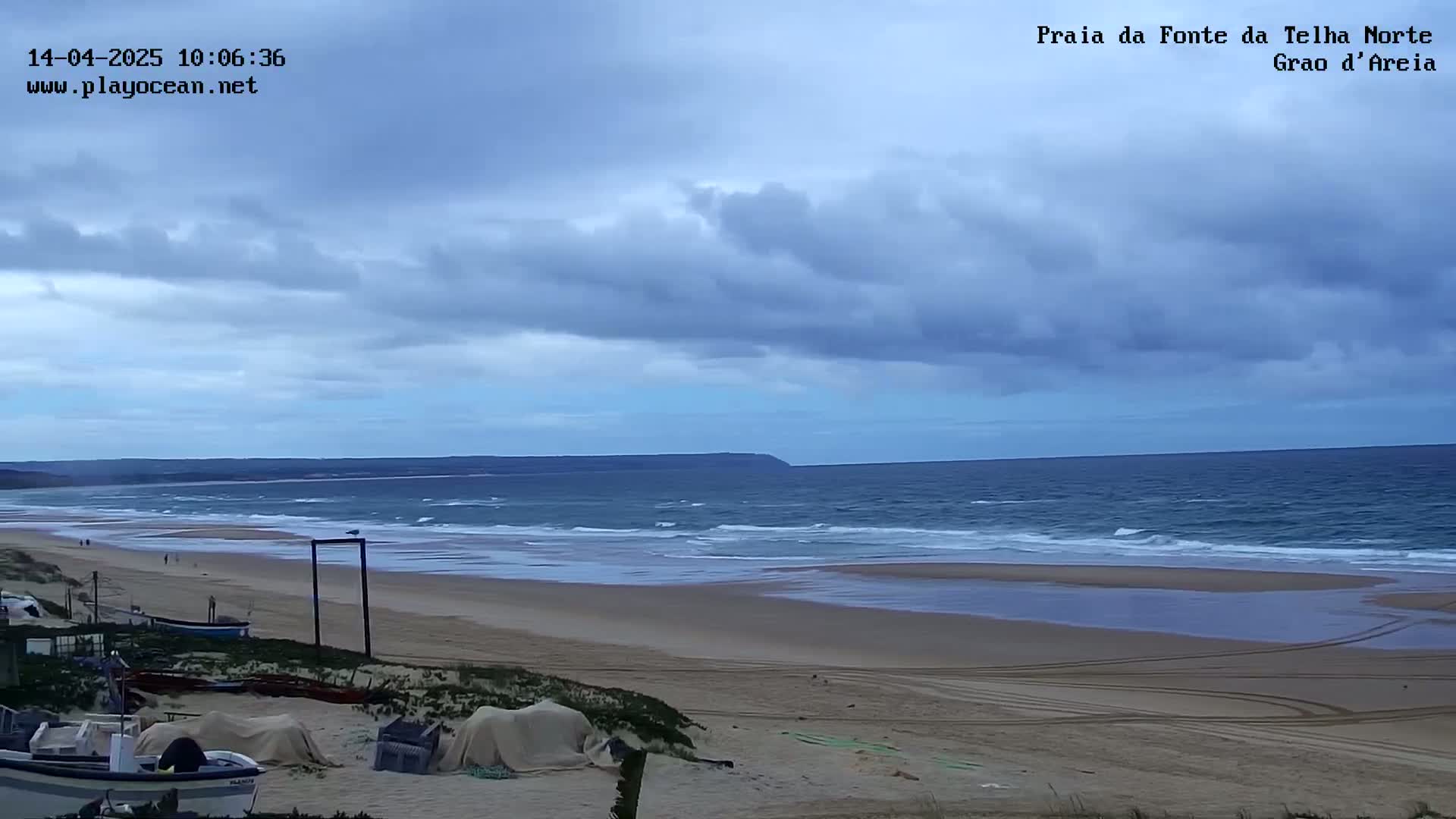 A wide sandy beach stretches out to a somewhat choppy ocean under a mostly cloudy sky.