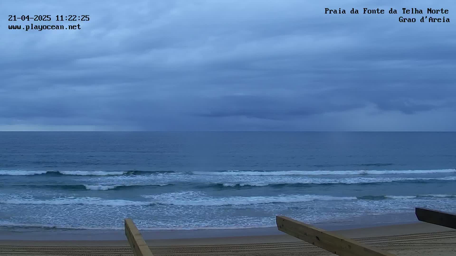 A sandy beach with gentle waves rolls onto the shore under a mostly cloudy sky.