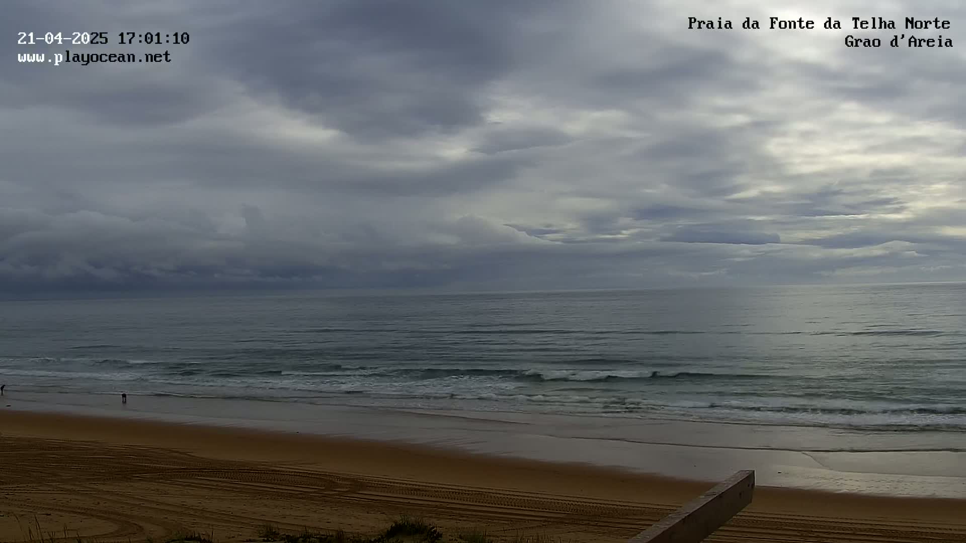 A sandy beach with a calm ocean under a mostly cloudy sky.