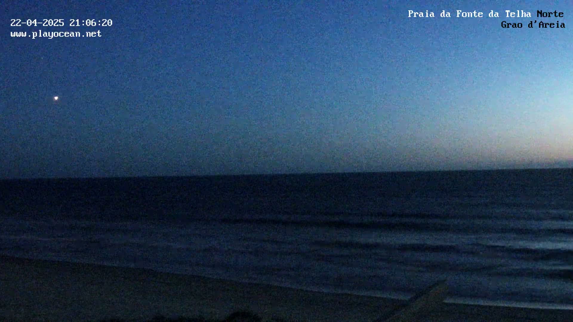A dark blue ocean meets a twilight sky above a sandy beach.