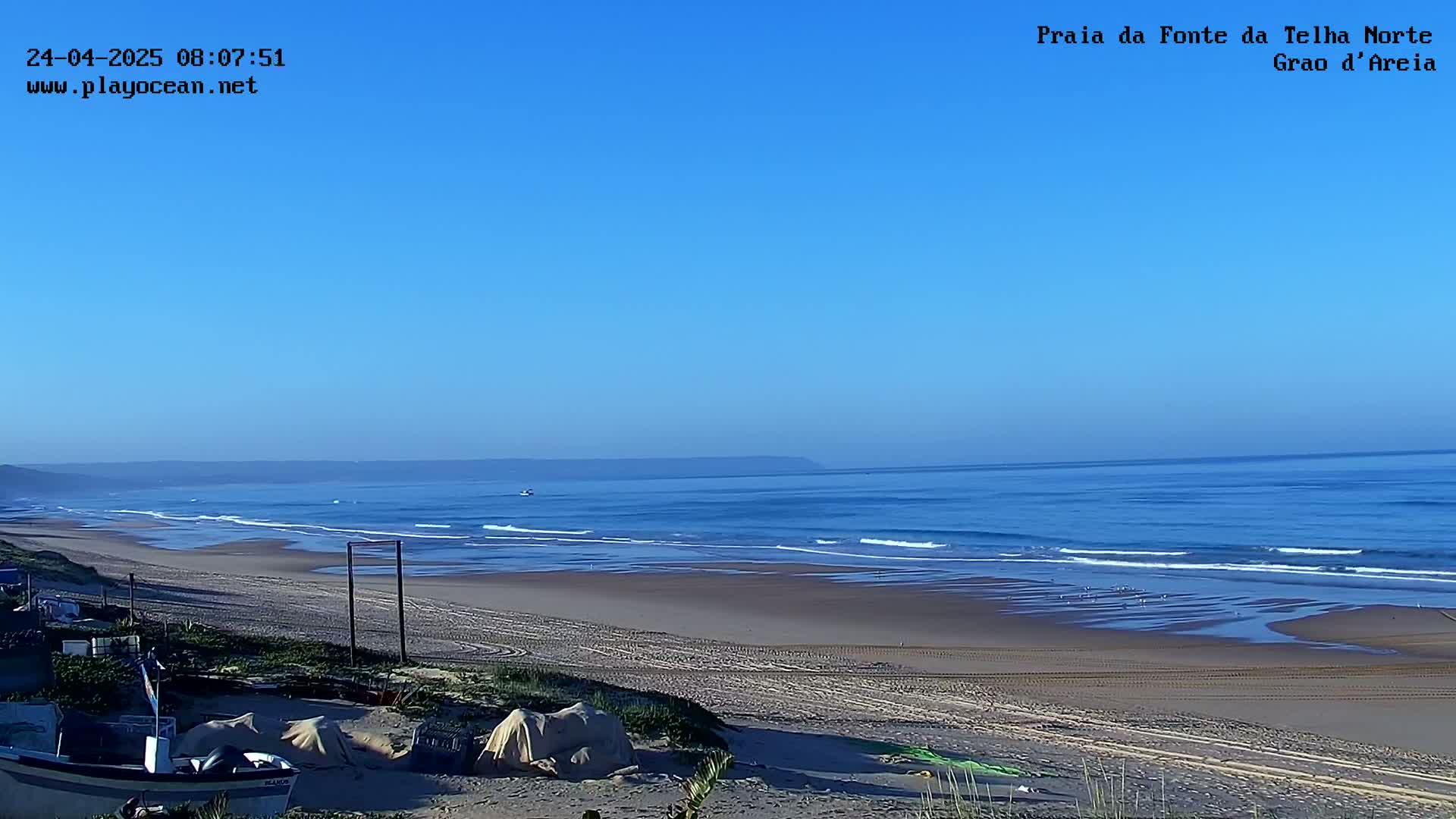 A sandy beach stretches to a calm ocean under a clear blue sky.