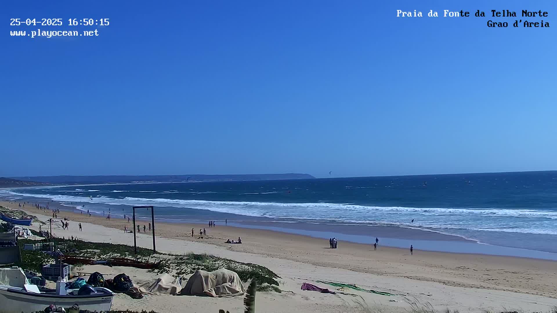 A sandy beach with people enjoying a sunny day, with blue ocean waves breaking along the shore under a clear blue sky.