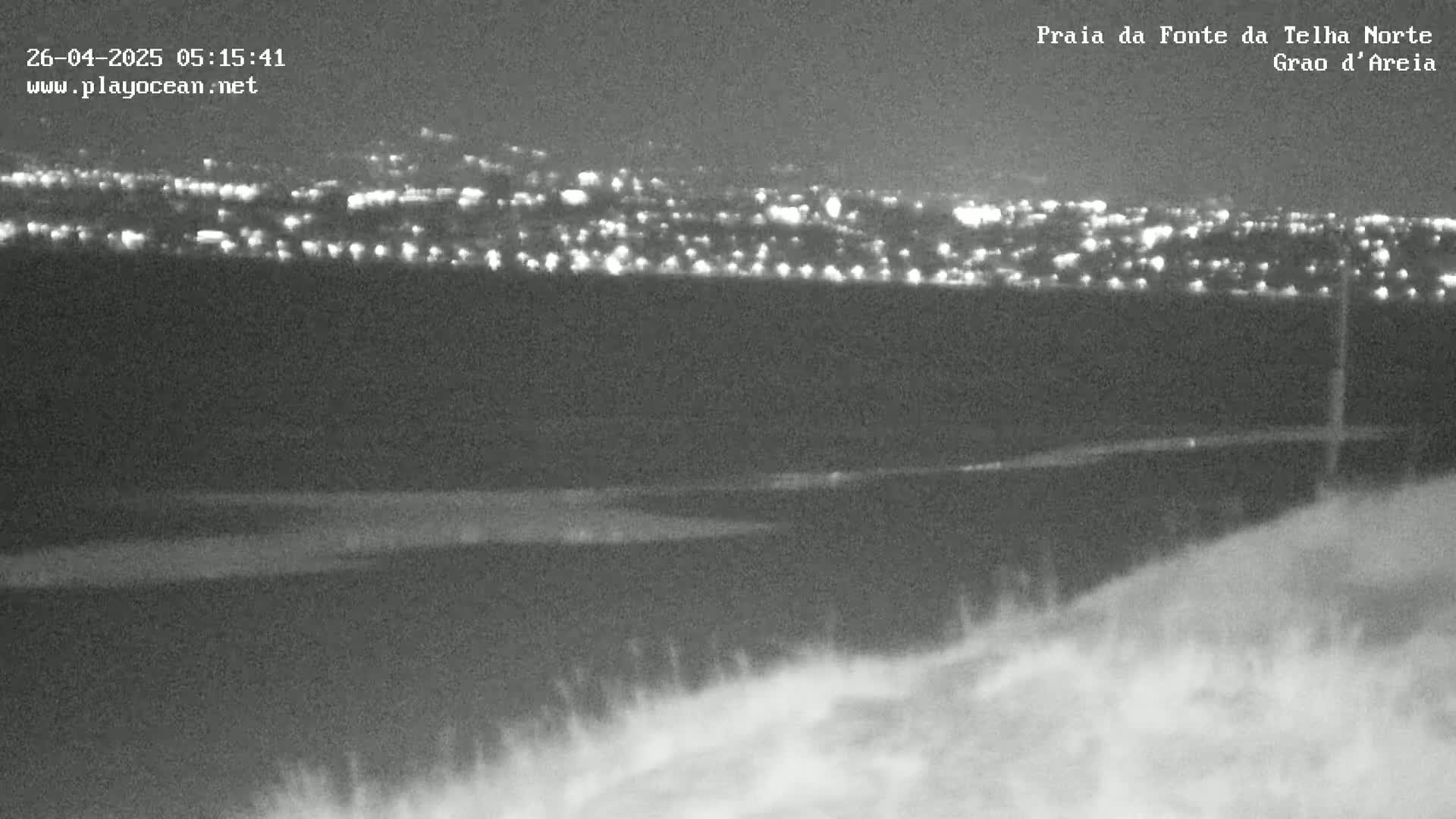 A nighttime, low-light view of a distant city illuminated by lights, seen from a vantage point over dark land.