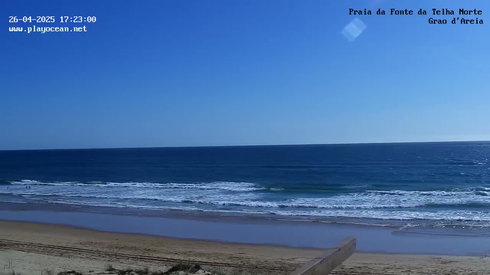 A sandy beach with gentle waves rolling onto the shore under a clear blue sky.