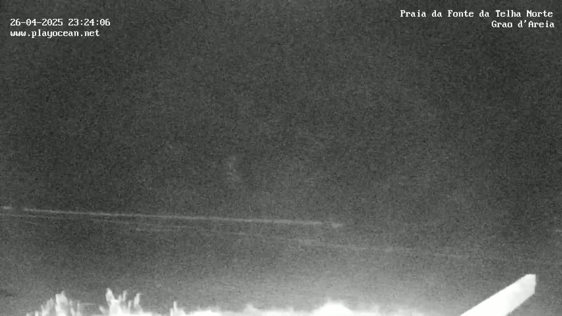 A low-light, nighttime image shows a dark, mostly featureless landscape with a faint horizontal line possibly representing a shoreline or road.